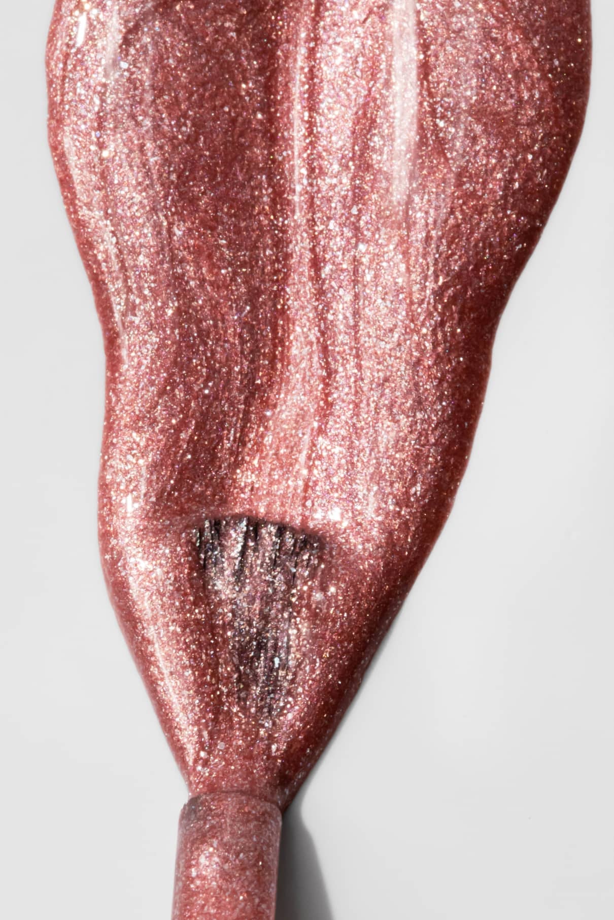 Nahaufnahme eines Pinsels, mit dem gitti no. 203, ein kupferfarbener Metallic-Nagellack, auf eine glatte, helle Oberfläche.
