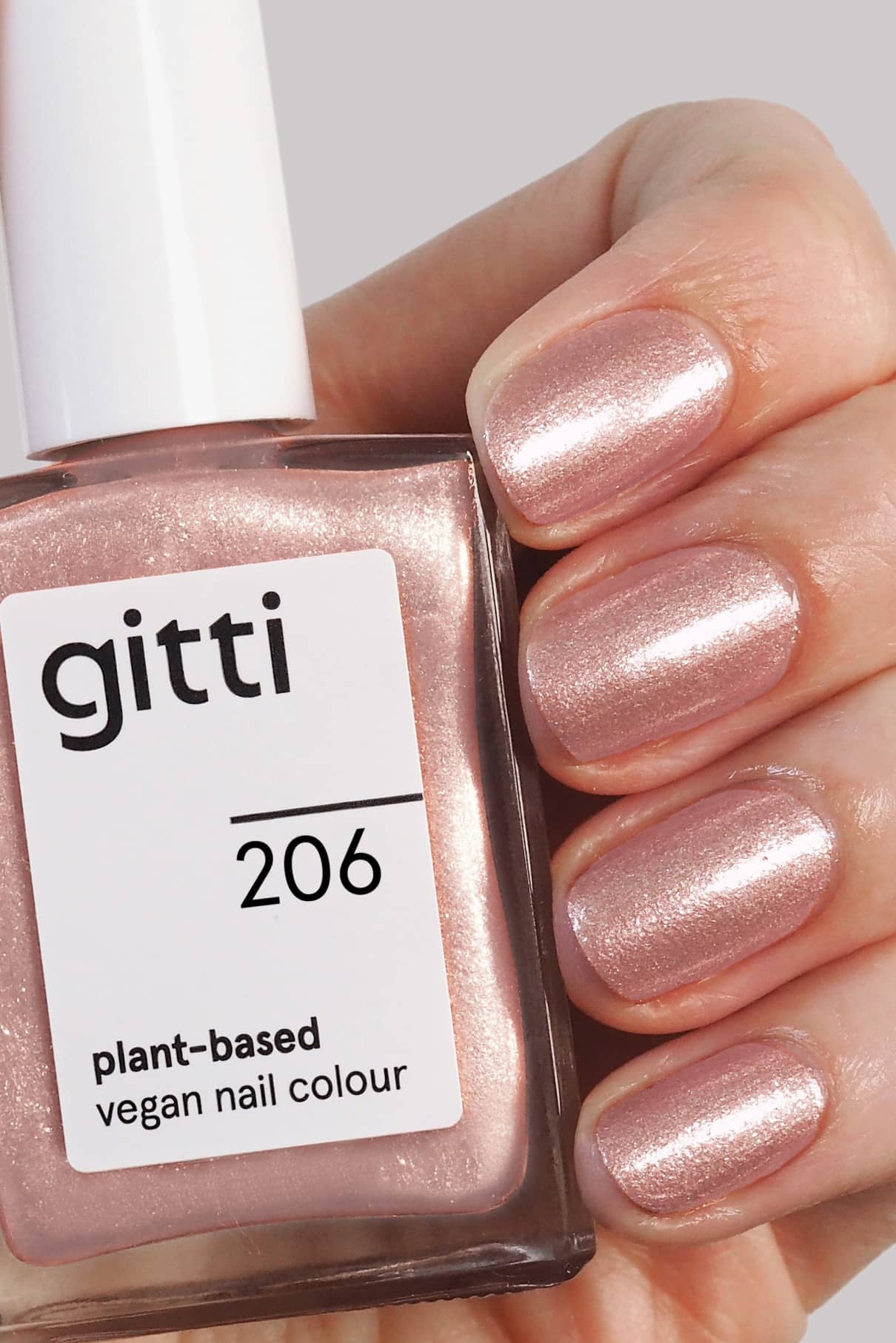 Eine Hand mit hellrosa schimmernden Nägeln hält eine Flasche von gitti no. 206, eine vegane Nagelfarbe auf pflanzlicher Basis in Rosaton-Glitzervariante, die perfekt für jede Gelegenheit ist.