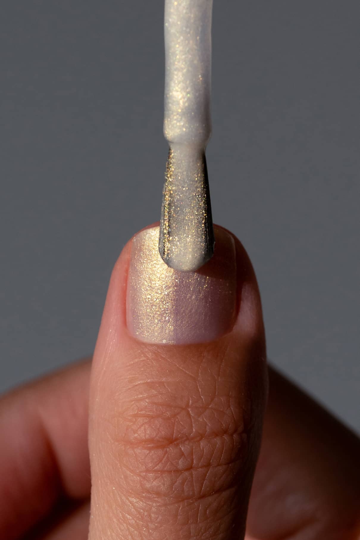 Eine Nahaufnahme eines Fingernagels, der mit gitti no. 207, einem schimmernden hellen Lack, mit einem Pinsel lackiert wird und ein eleganter irisierender Schimmer auf dem weißen Nagel entsteht.