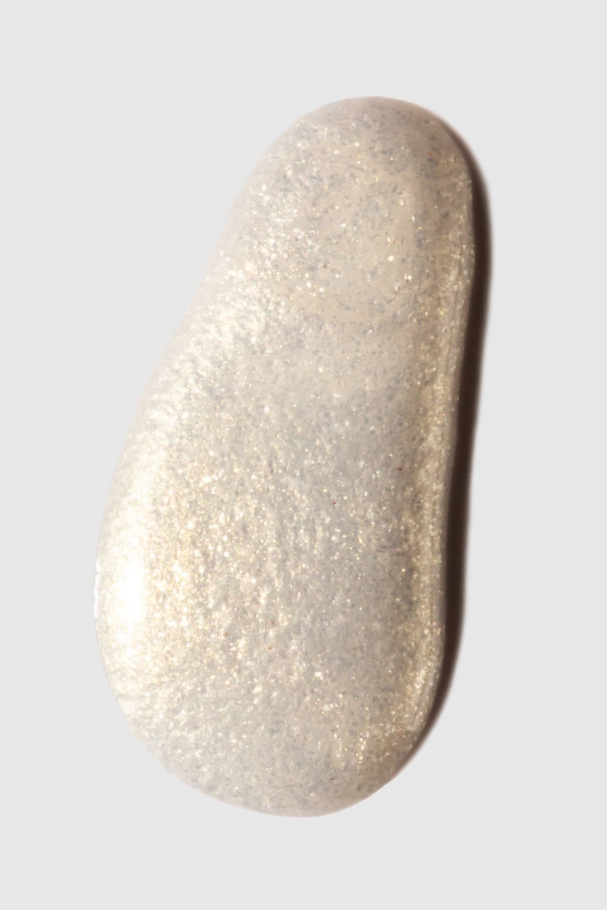 Ein unregelmäßiges, ovalförmiges Muster von gitti no. 207 in perlweißem Gel oder Creme schimmert mit einem irisierenden Glanz auf einem schlichten hellgrauen Hintergrund.