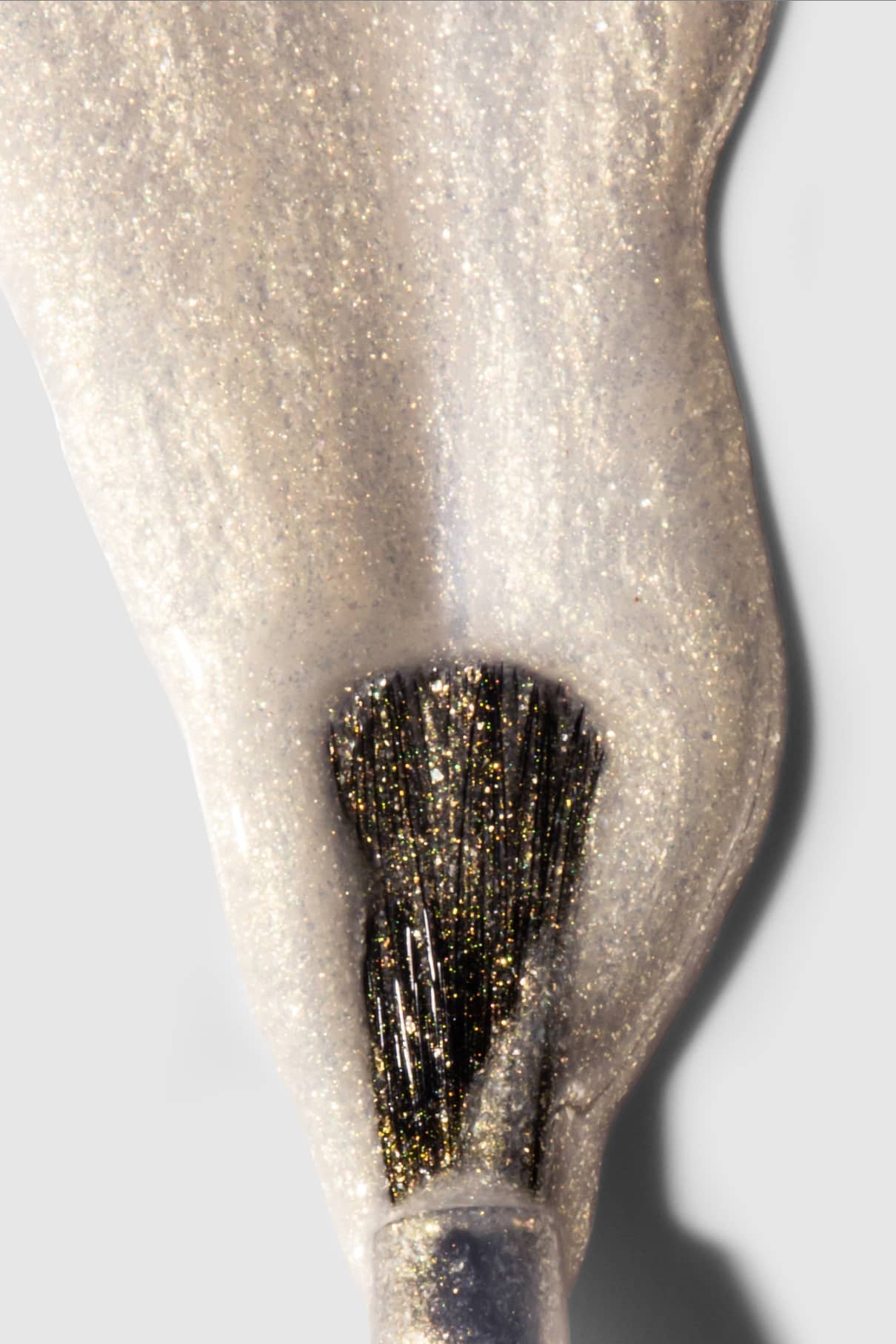 Nahaufnahme eines Nagellackpinsels, der gitti no. 207, ein gold-bläulicher, irisierender Schimmer-Lack, auf eine glatte, helle Oberfläche.