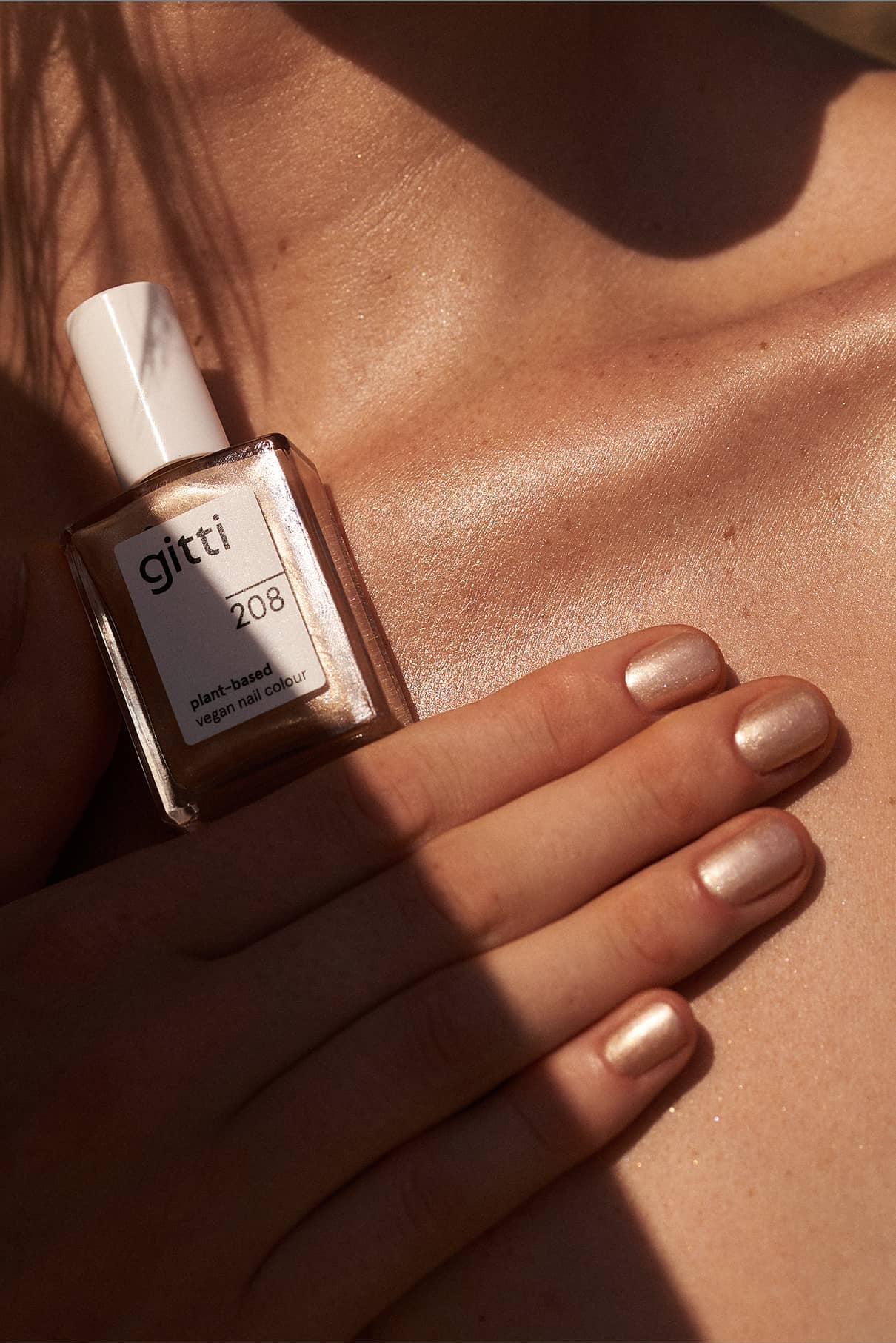 Eine Hand mit metallischem Nude-Lack in einem schimmernden Goldton hält eine Flasche gitti no. 208 pflanzlicher, veganer Nagellack gegen die nackte Haut.