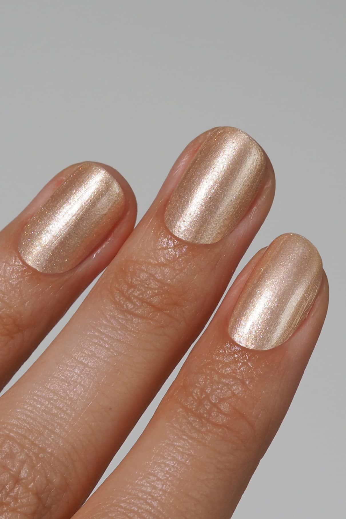 Eine Nahaufnahme von drei Fingern mit kurzen, sauber manikürten Nägeln, die mit gitti no. 208, einem schicken Metallic-Lack in Champagner oder hellem Gold.