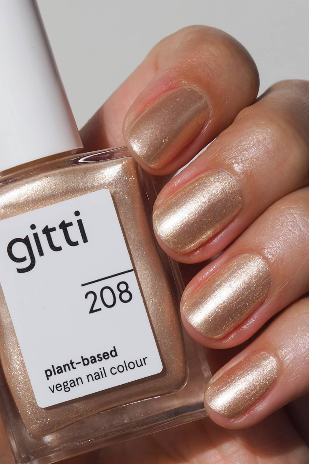 Eine Hand mit sauber manikürten, in einem funkelnden Goldton lackierten Nägeln hält eine Flasche gitti no. 208 pflanzlicher, veganer Nagellack.