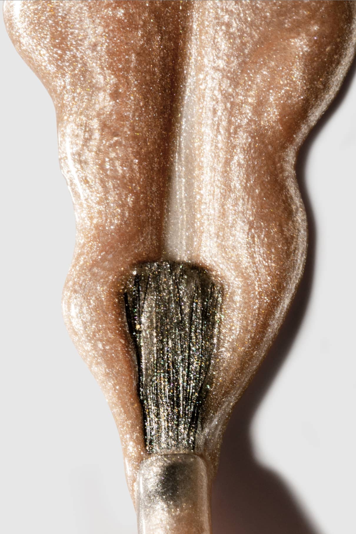 Nahaufnahme eines Nagellackpinsels, der mit gitti no. 208, einem metallisch schimmernden, goldbeigen Nagellack, vor weißem Hintergrund.