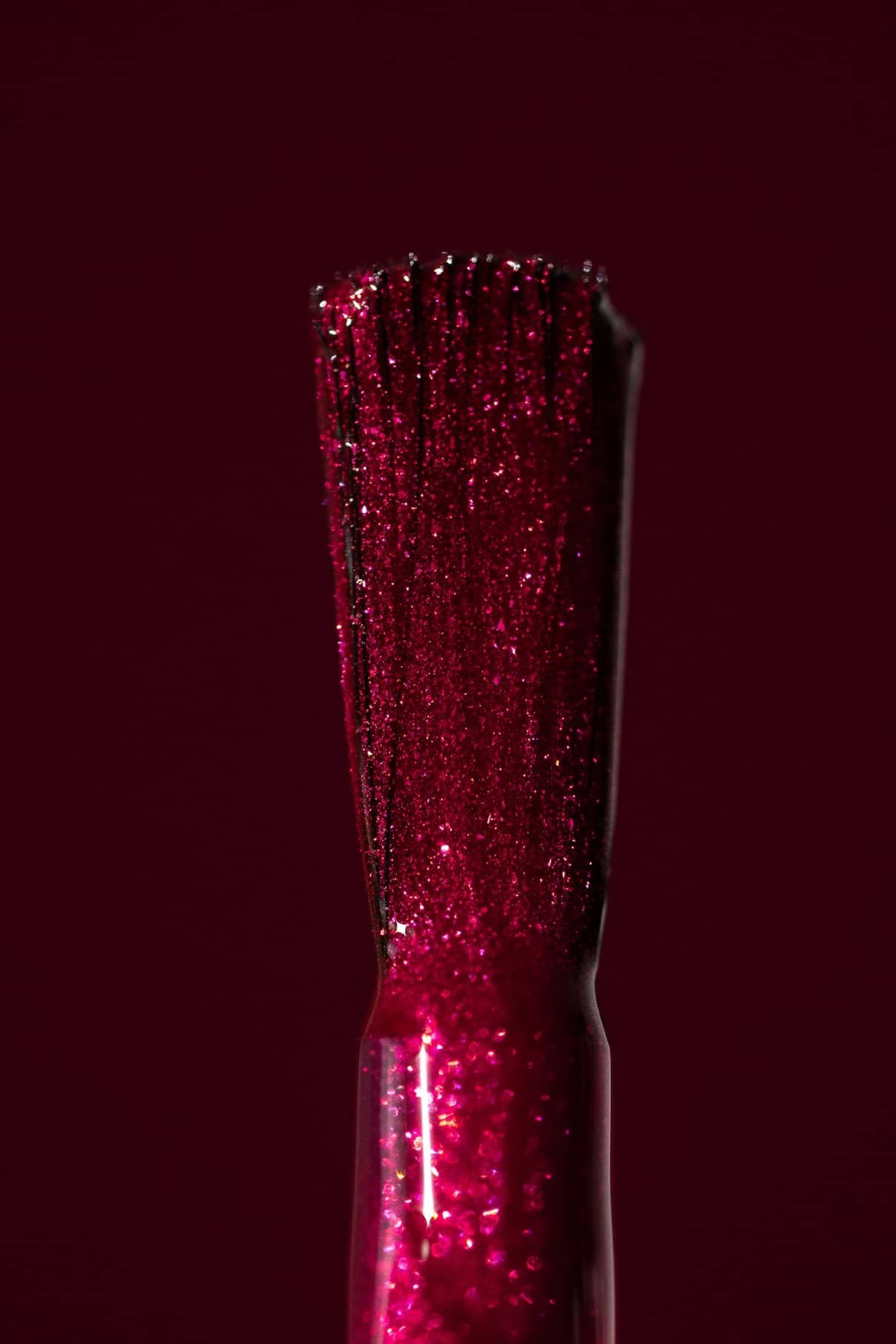 Nahaufnahme eines gitti no. 212 Pinsel mit rotem Glitzerlack vor einem passenden Hintergrund in tiefem bierigem Rot mit metallischem Schimmer.