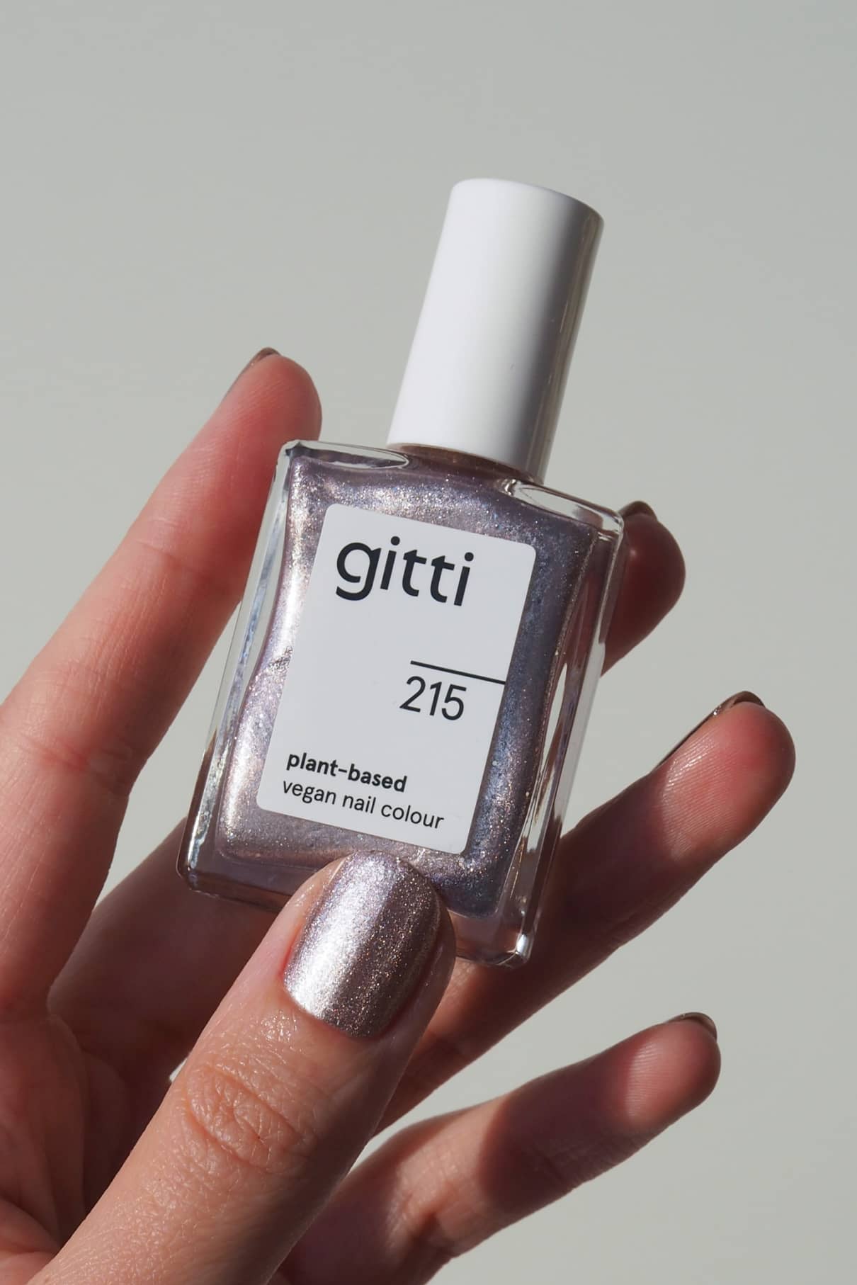 Eine Hand hält eine Flasche mit gitti no. 215 pflanzlicher, veganer Nagellack in zartem Rosa, mit passender Farbe auf den Fingernägeln.