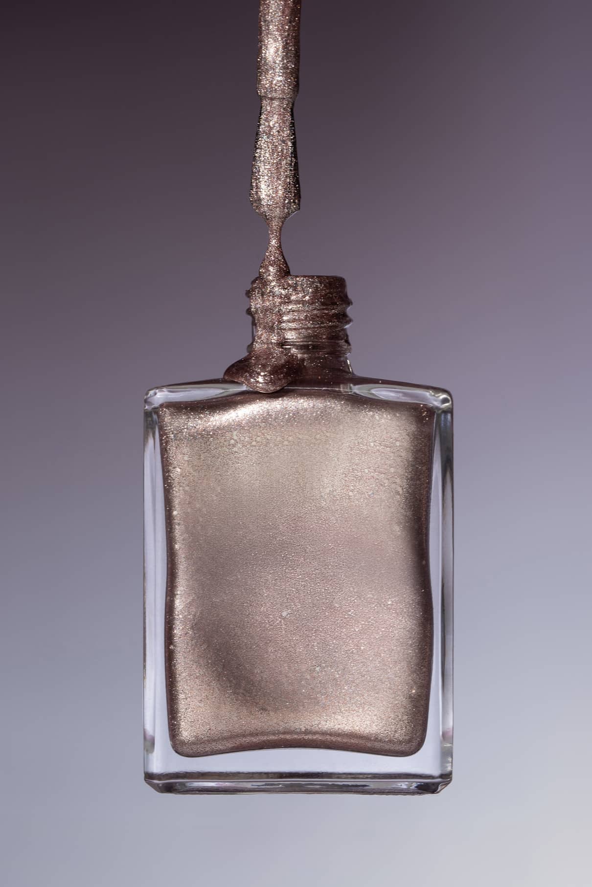 Eine Flasche gitti no. 215 Nagellack, wobei der Pinsel herausgezogen wird und der rosa schimmernde Lack zurück in die Flasche tropft.