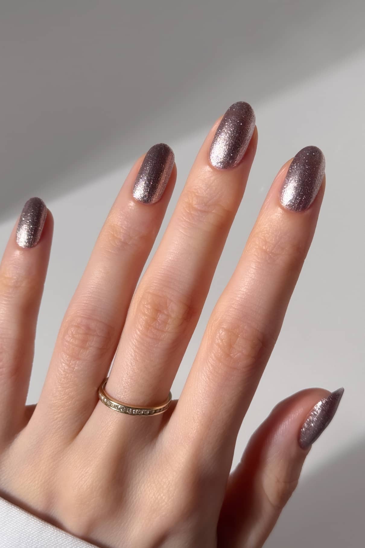Eine Hand mit kurzen, ovalen Nägeln, die mit gitti no. 215, einem schimmernden rosa Lack, mit einem einfachen Goldring am Ringfinger.