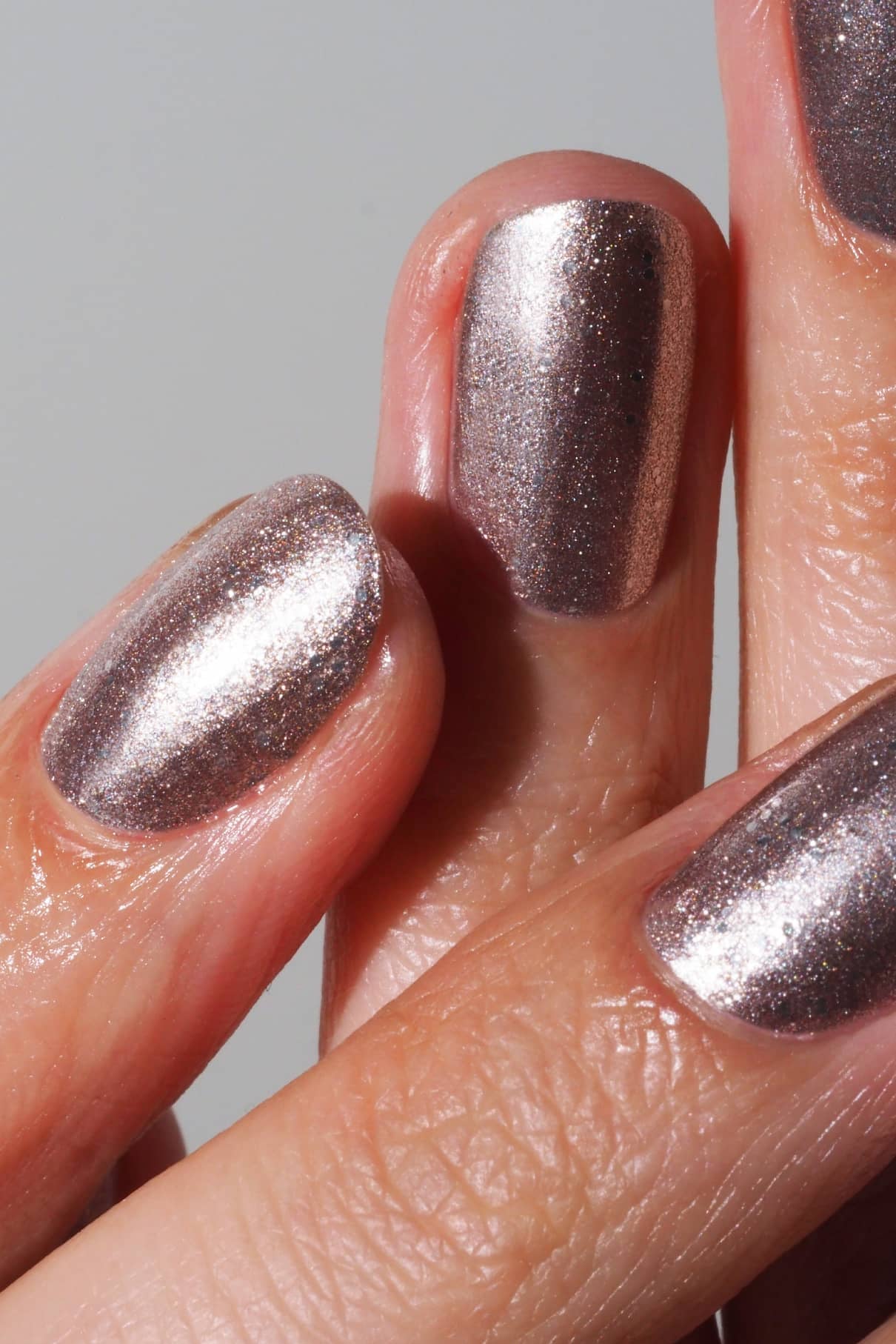 Nahaufnahme von drei gepflegten Fingern, jeder mit schimmerndem rosa und silberfarbenem Nagellack lackiert, mit gitti no. 215.