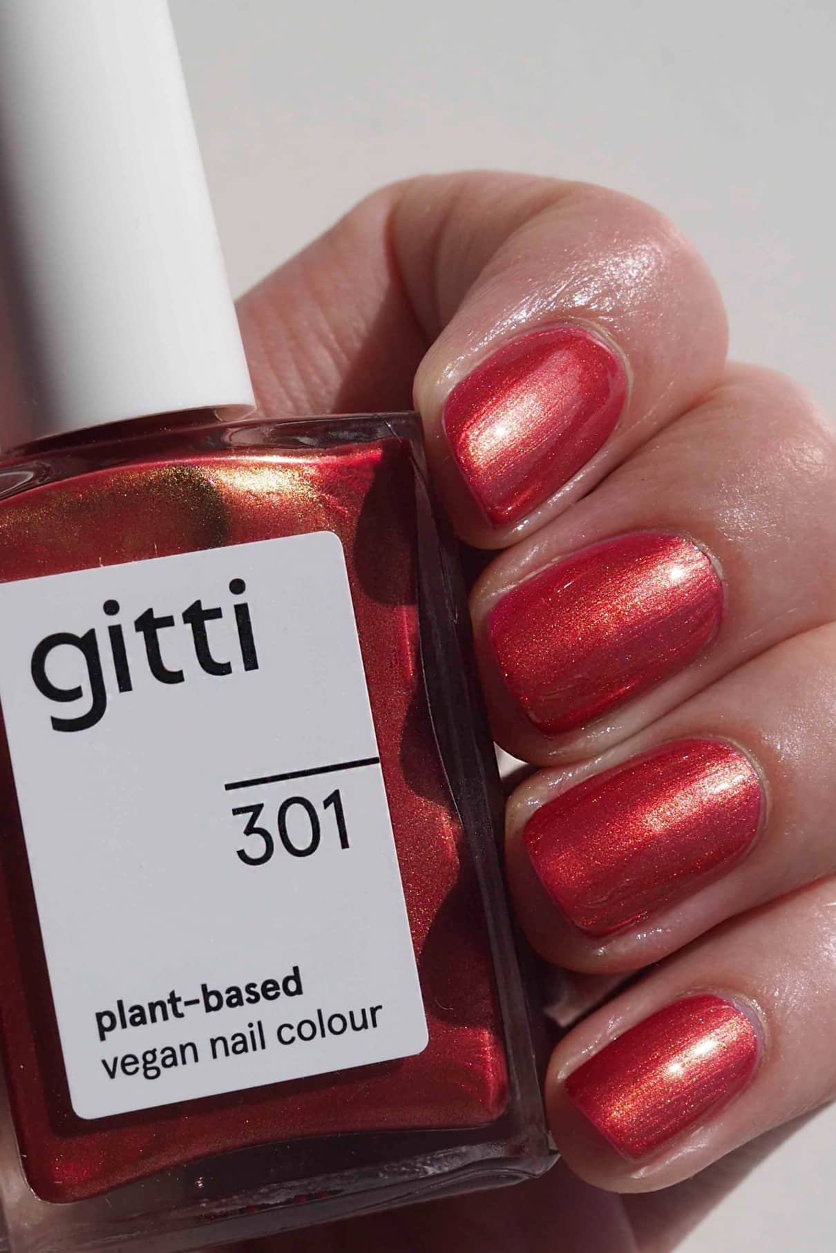 Eine Hand mit Rotton-Metallic-Nagellack hält eine Flasche mit der Aufschrift gitti no. 301 pflanzliche vegane Nagelfarbe.