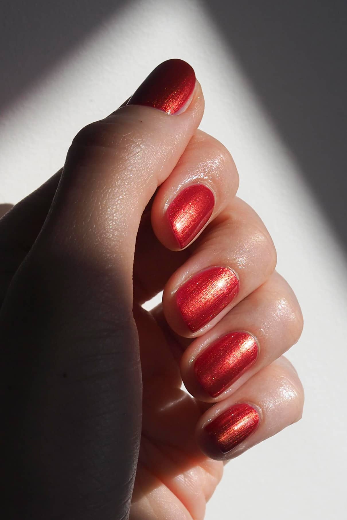 Nahaufnahme einer Hand mit sauber manikürten Nägeln, die mit gitti no. 301, einem glänzenden roten Metallic-Lack, bei natürlichem Licht gezeigt.