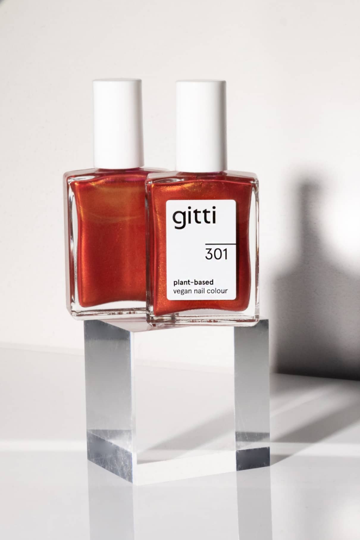 Zwei Flaschen gitti no. 301 pflanzliche vegane Nagelfarbe in leuchtendem Rot, ausgestellt auf einem durchsichtigen Acrylblock vor weißem Hintergrund.