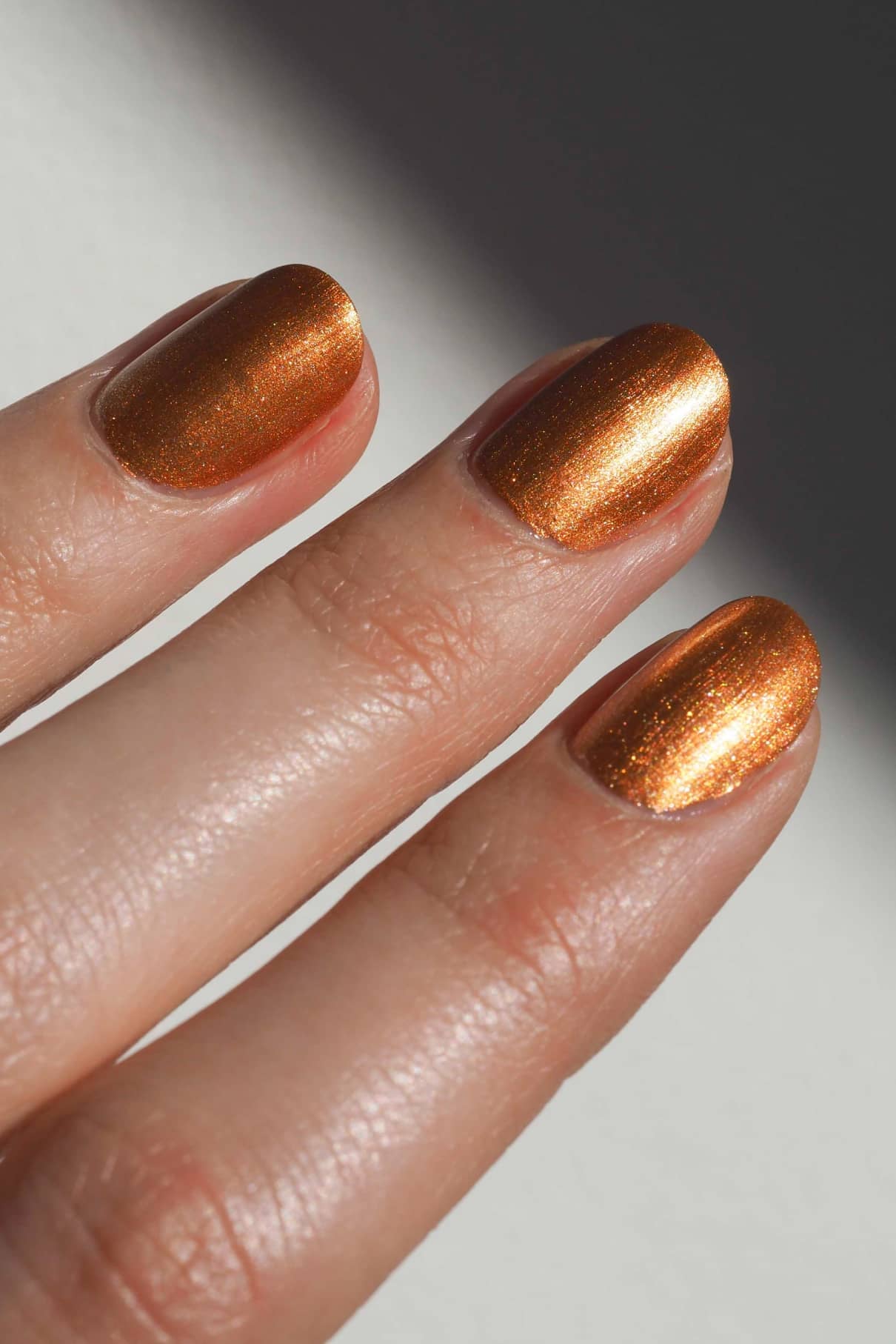 Nahaufnahme von drei Fingern mit metallisch-orangem Nagellack im auffälligen Farbton gitti no. 302.