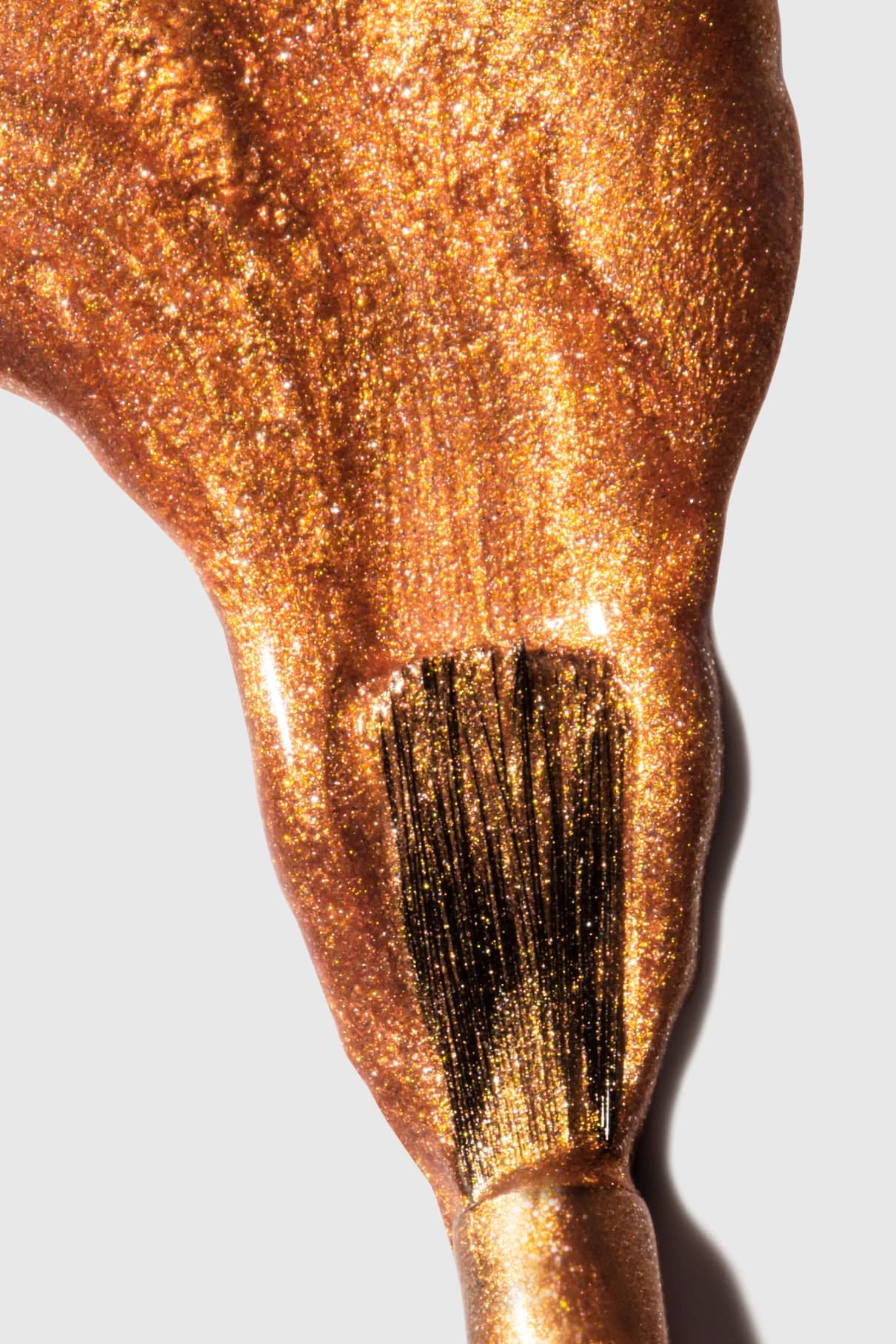 Nahaufnahme eines Pinsels, mit dem gitti no. 302 Nagellack in einem auffälligen Metallic-Bronzeton-Farbton auf eine weiße Fläche auf.