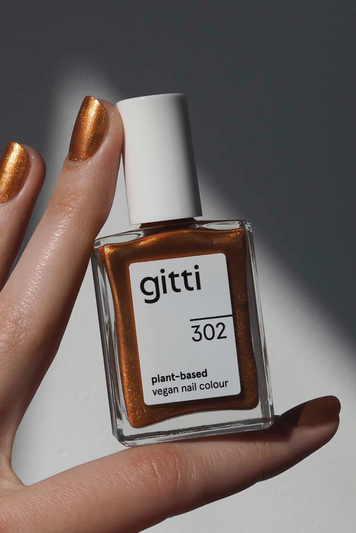 Eine Hand mit bronzefarbenem Metallic-Nagellack hält ein Fläschchen mit gitti no. 302 pflanzlicher veganer Nagellack in einem passenden Metallic-Ton.
