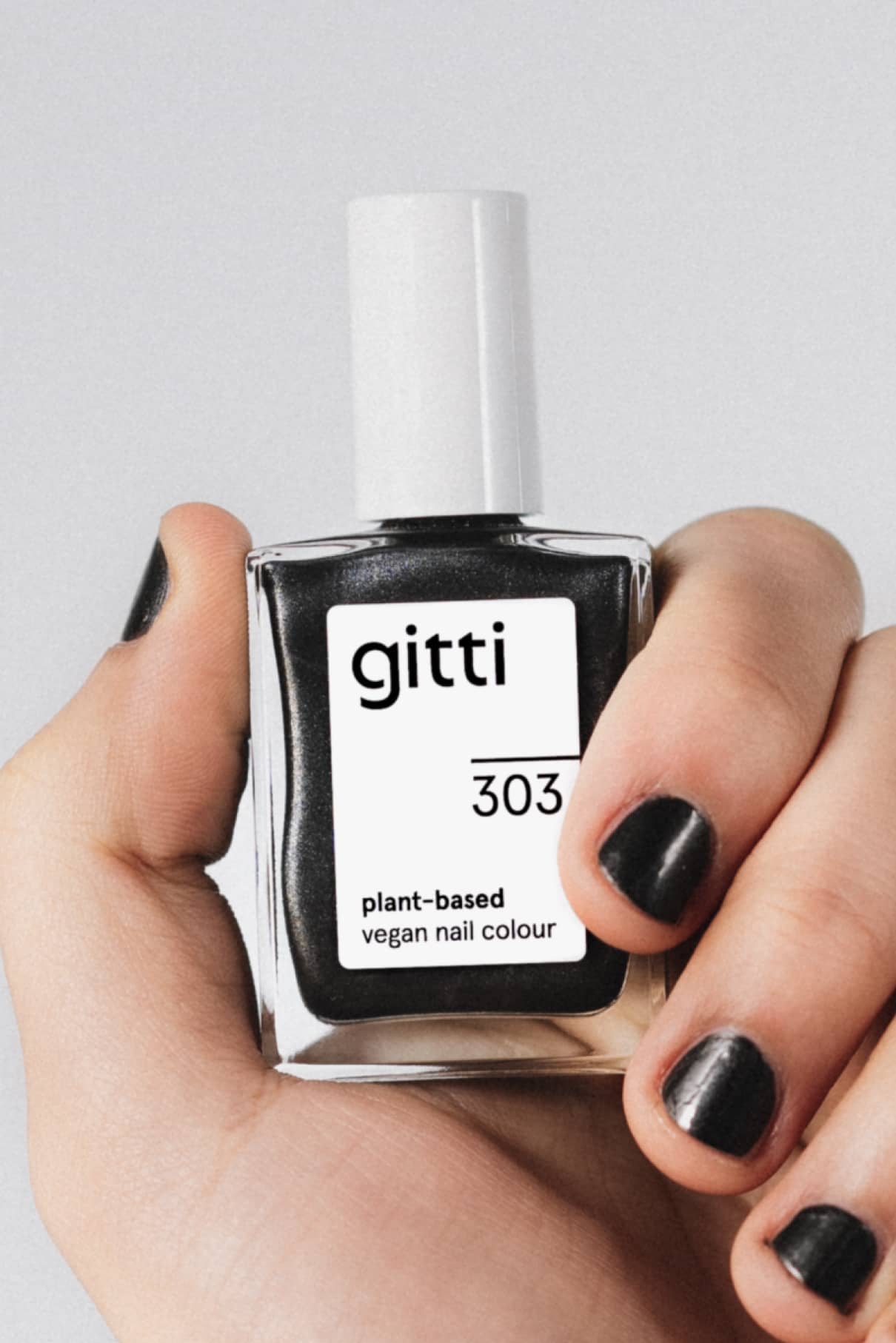 Eine Hand hält eine Flasche mit gitti no. 303 pflanzliche vegane Nagelfarbe in Schwarz; die Nägel sind mit demselben intensiven schwarzen Lack mit silbrigem Metallic-Finish lackiert.