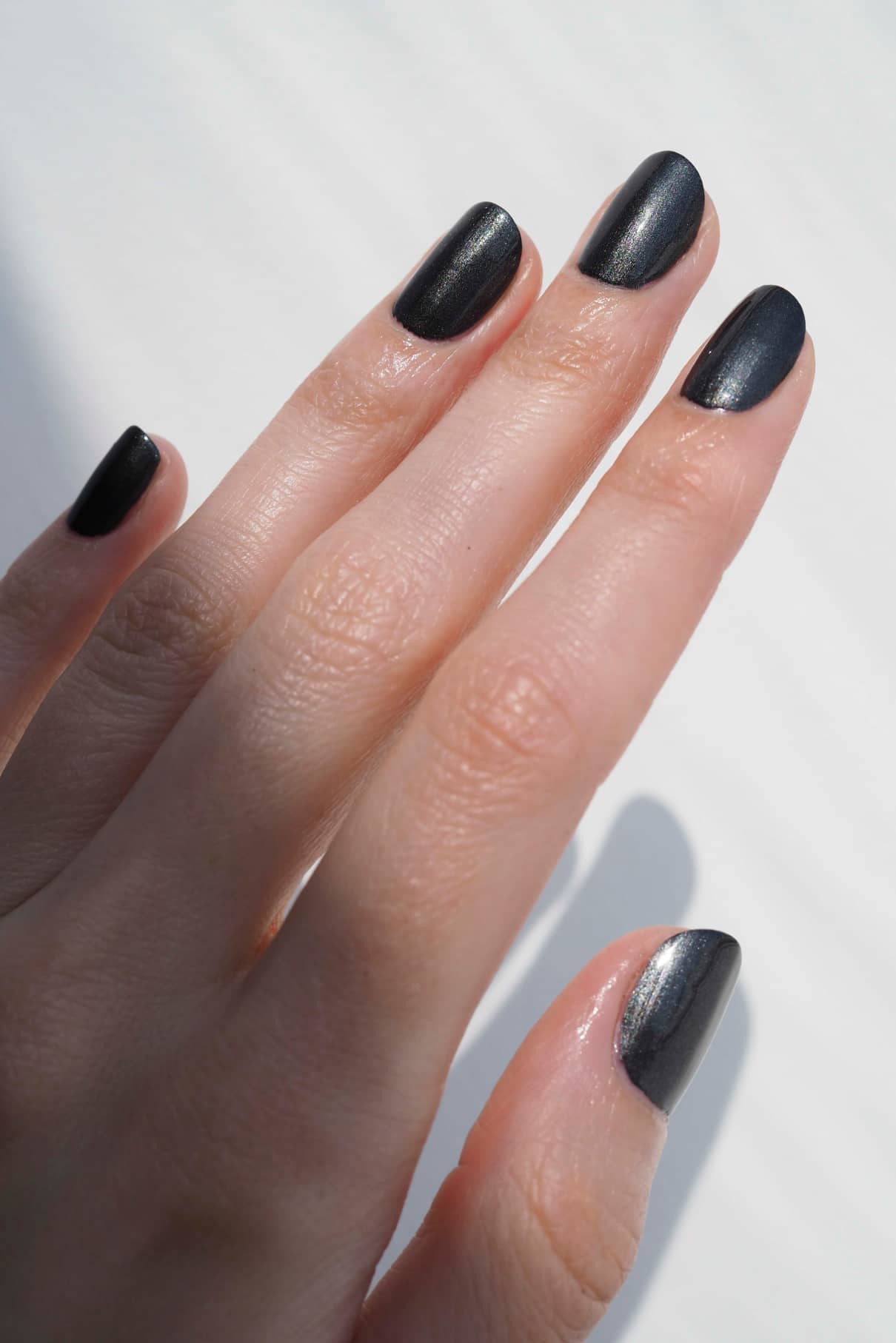 Eine Hand mit sauber manikürten Nägeln, lackiert mit gitti no. 303, einem schwarz-silbrigem Metallic-Finish Nagellack.