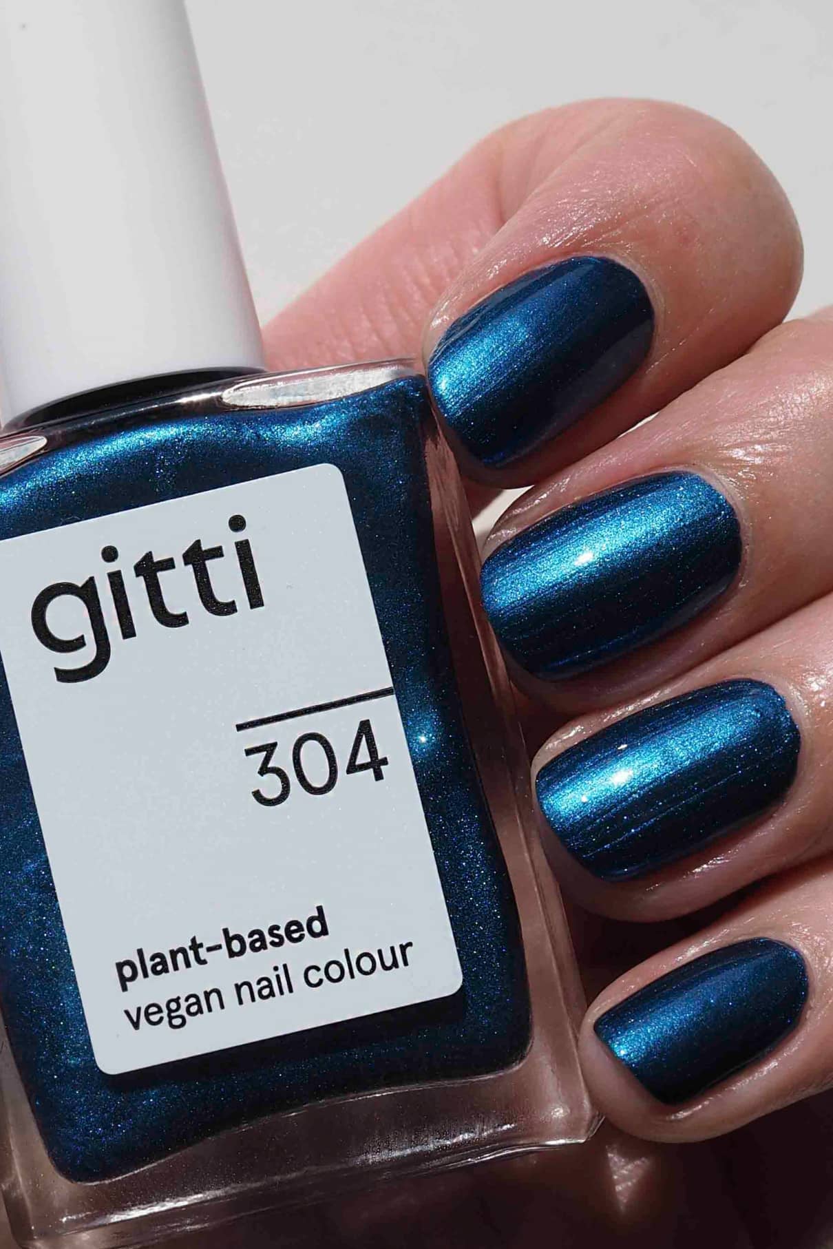 Eine Hand mit in kräftigem Metallic-Blau lackierten Fingernägeln hält eine Flasche gitti no. 304 pflanzlicher veganer Nagelfarbe im passenden Farbton.