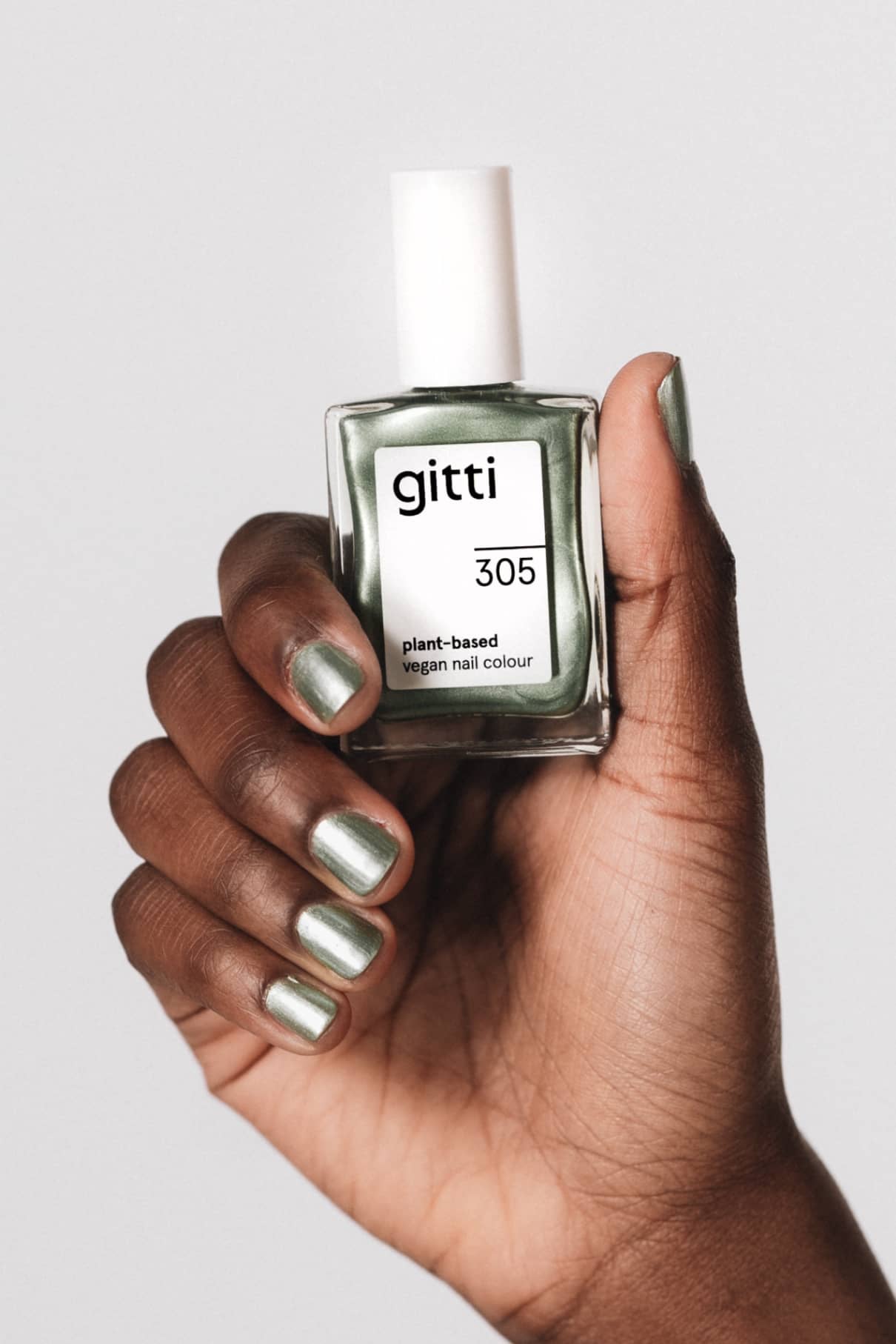 Eine Hand mit grünem Metallic-Nagellack hält eine Flasche mit der Aufschrift gitti no. 305, eine vegane Nagelfarbe auf Pflanzenbasis mit Metallic-Finish.