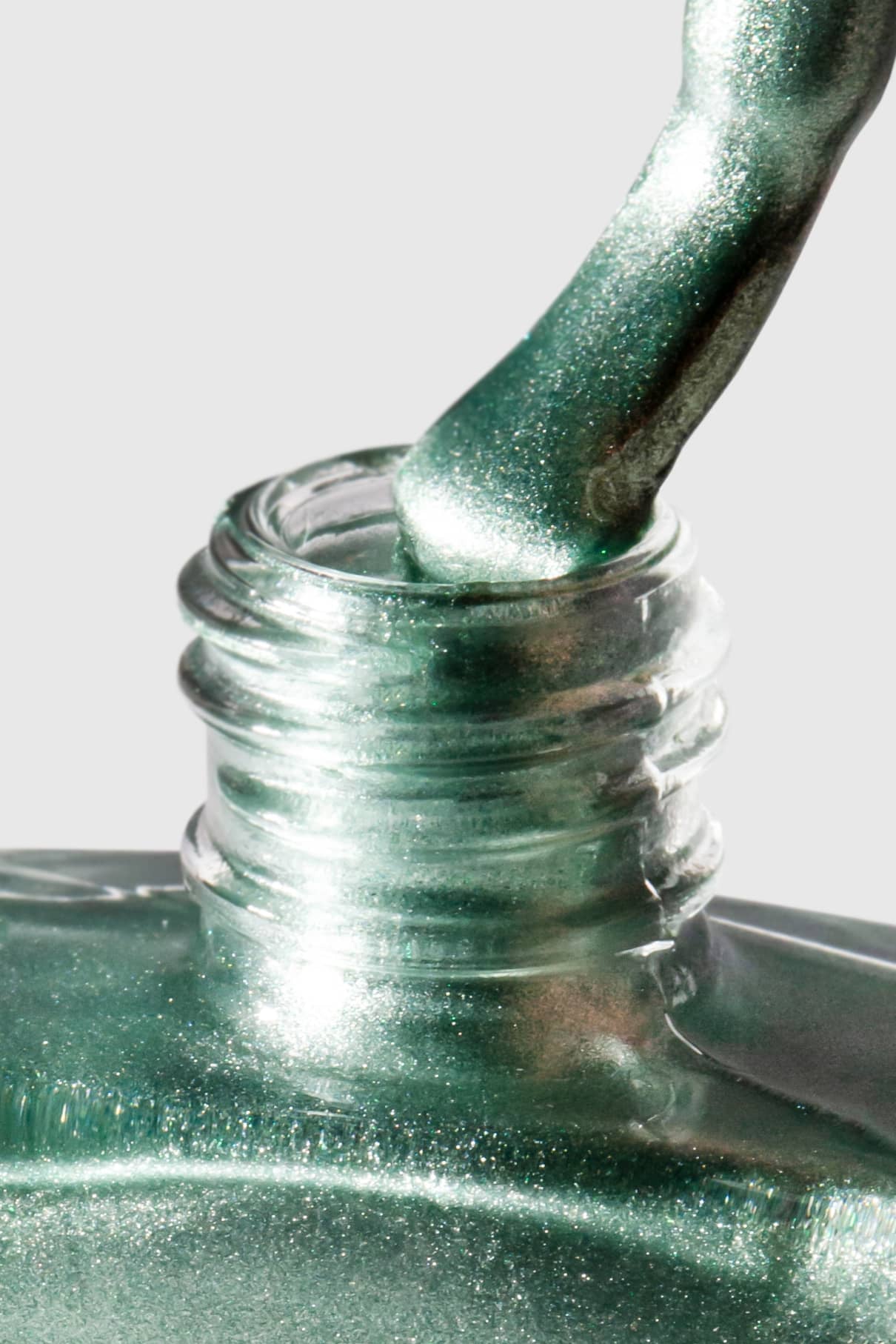 Nahaufnahme von gitti no. 305, einer metallicgrünen Nagellackflasche, mit dem Pinsel, der den Lack in die offene Flasche zurücktropfen lässt, vor einem hellen Hintergrund.