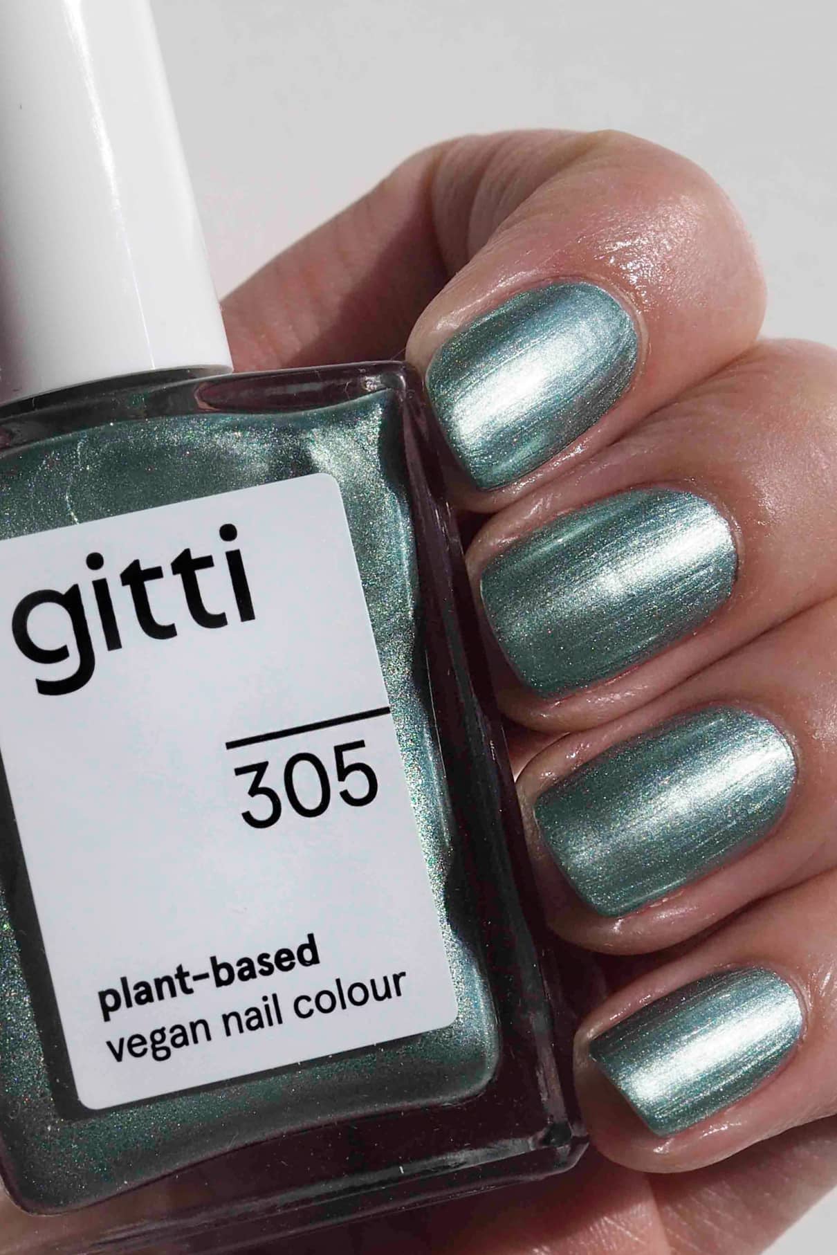Eine Hand mit grünem Nagellack in der Metallic-Version hält eine Flasche mit der Aufschrift gitti no. 305 vegane Nagellackfarbe auf Pflanzenbasis.