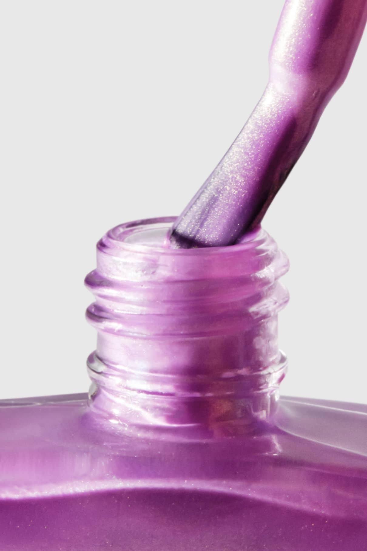 Nahaufnahme eines Pinsels, der in eine offene Flasche mit gitti no. 306, einem schimmernden lila Nagellack mit metallisch-mauvefarbenem Finish und violettem Unterton, vor einem schlichten Hintergrund.