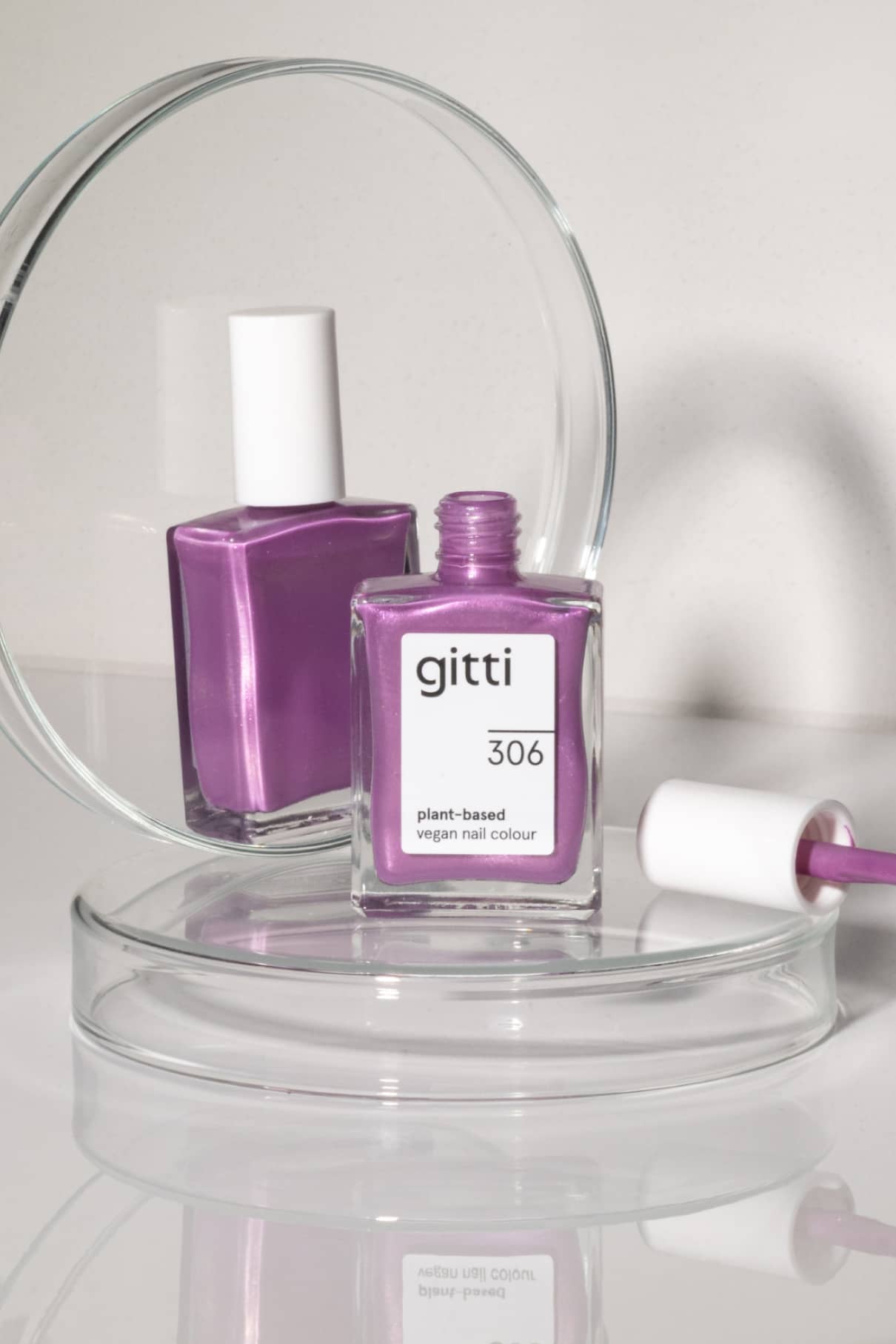 Eine Flasche gitti no. 306 pflanzlicher veganer Nagellack in einem violetten Farbton mit violettem Unterton steht vor einem Spiegel, daneben Pinsel und Kappe.