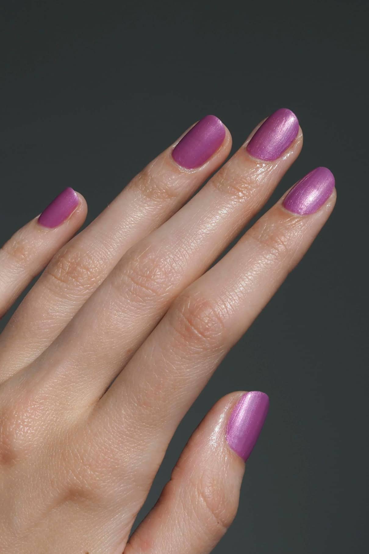 Eine Hand mit sauber manikürten Nägeln, lackiert in gitti no. 306, einem Metallic-Mauve-Ton mit violettem Unterton, vor einem schlichten dunklen Hintergrund.