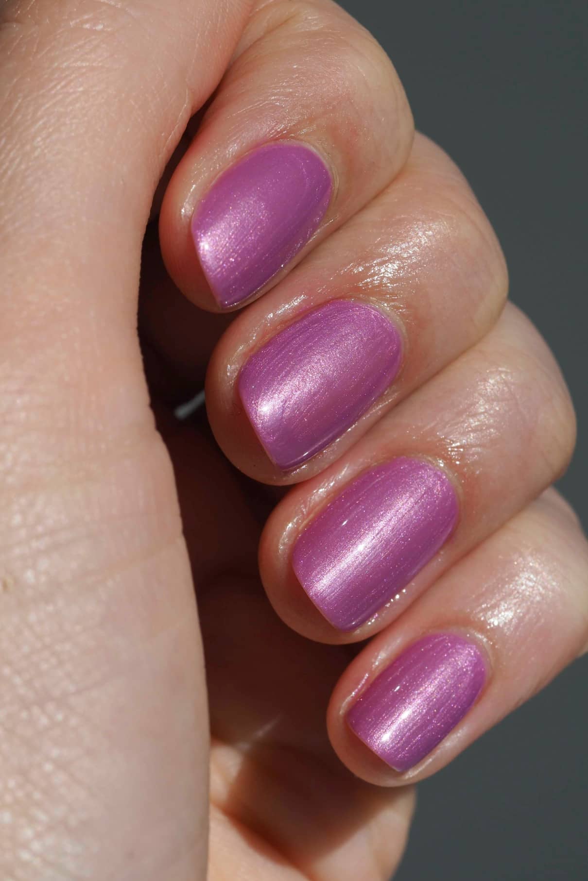 Eine Nahaufnahme einer Hand mit kurzen Nägeln, die mit gitti no. 306, einem schimmernden lavendellila Nagellack mit einer metallisch-mauvefarbenen Nuance und violetten Untertönen.