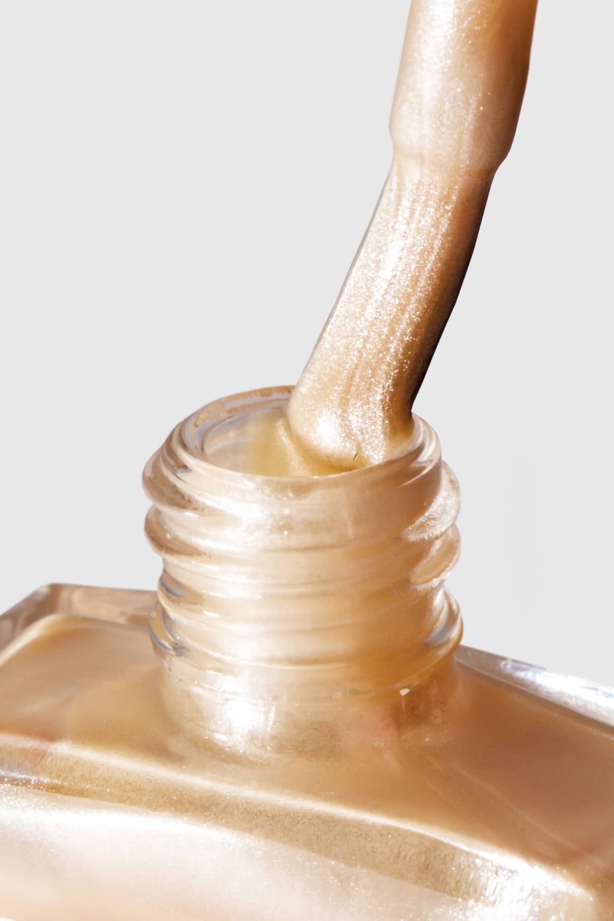 Eine Nahaufnahme eines Nagellackpinsels, der aus einer Flasche mit gitti no. 307, einem weichen, hellbeigen Farbton mit einem Hauch von metallischem Cremeschimmer.