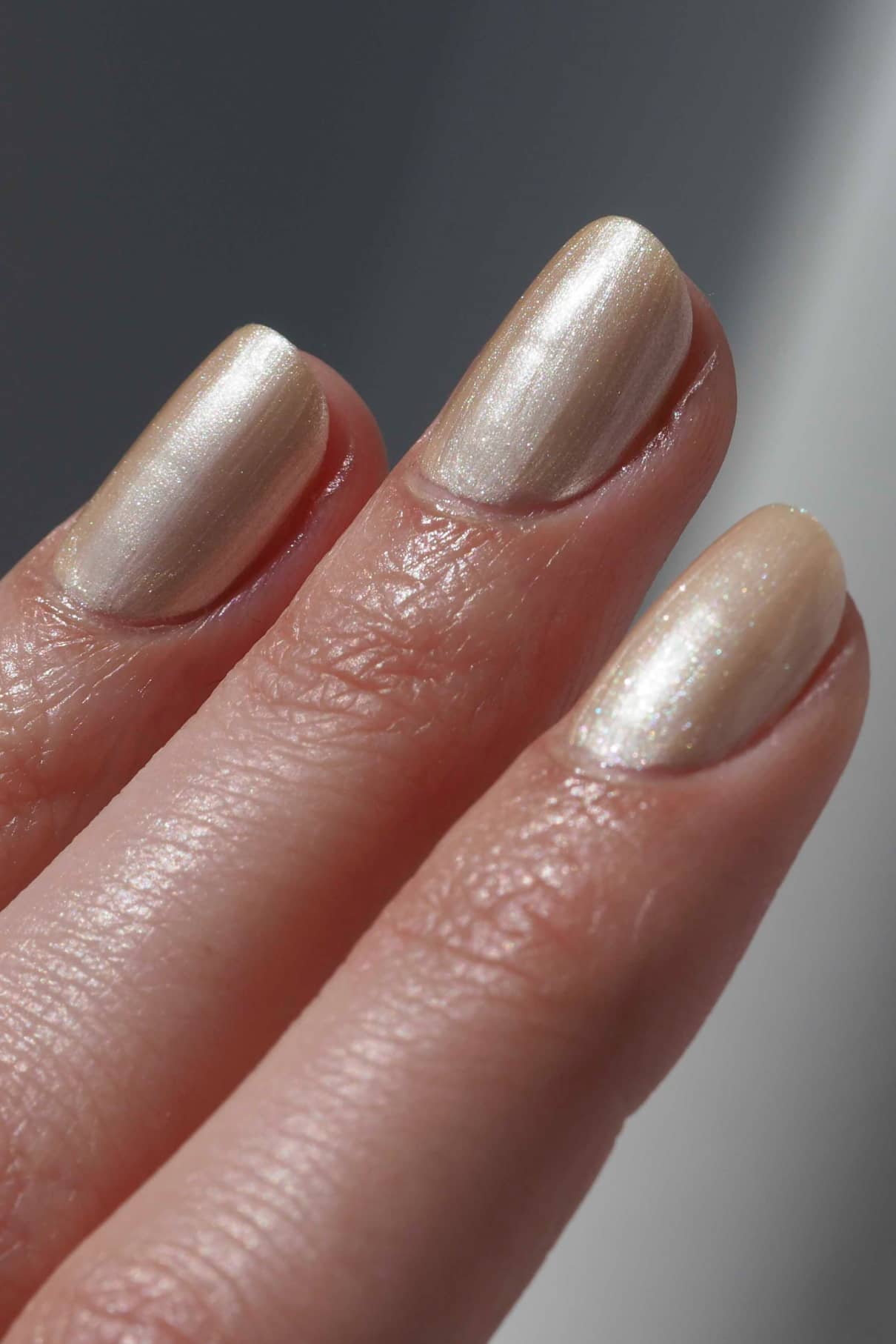 Nahaufnahme von drei Fingern mit kurzen, sauber manikürten Nägeln, die mit gitti no. 307, einem weichen Metallic-Creme-Nagellack in einem schimmernden, blassen Champagner-Roségold-Ton.