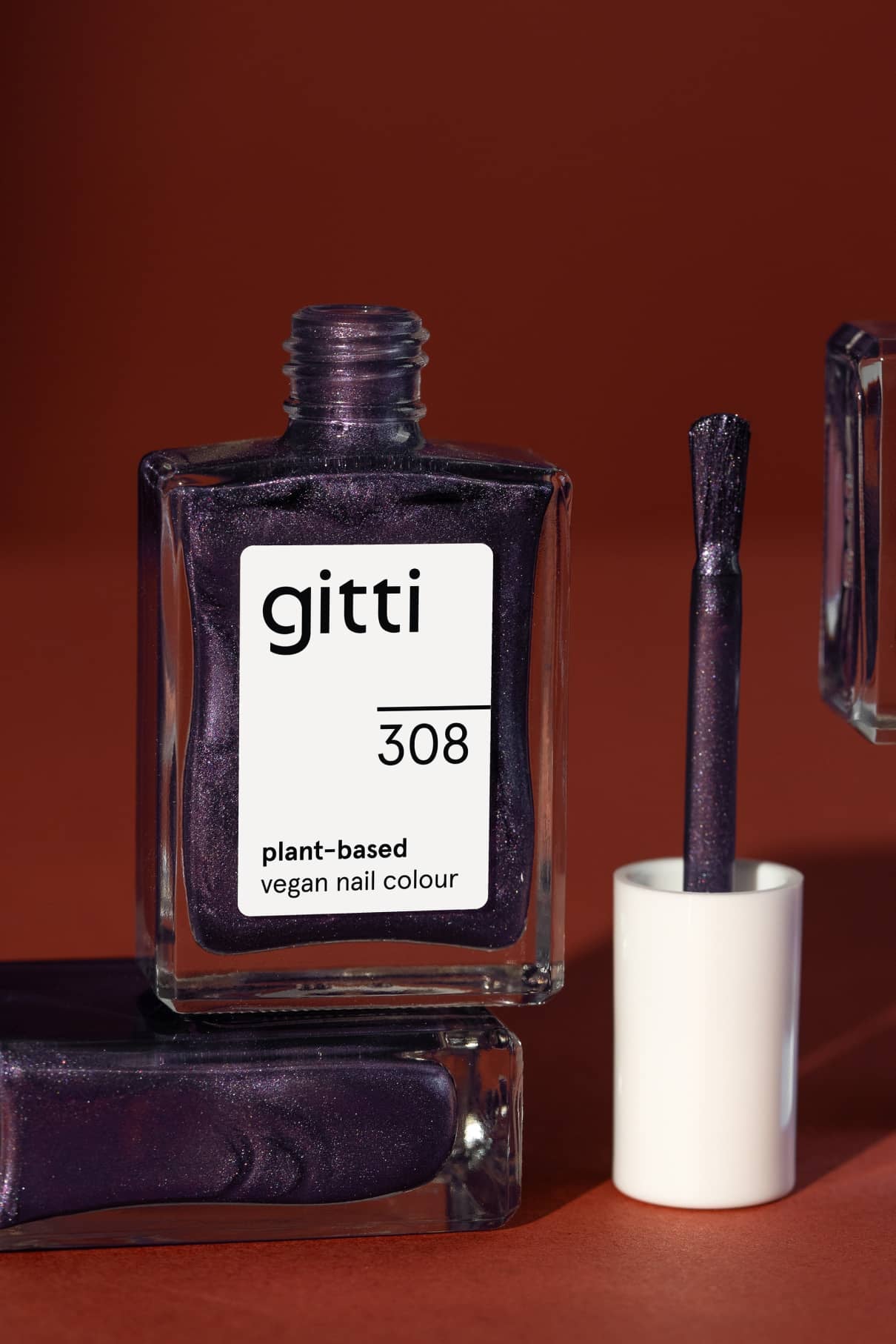 Eine Flasche gitti no. 308 pflanzlicher, veganer Nagellack mit metallischem Schimmer ist zusammen mit dem Pinselapplikator vor einem rotbraunen Hintergrund abgebildet.