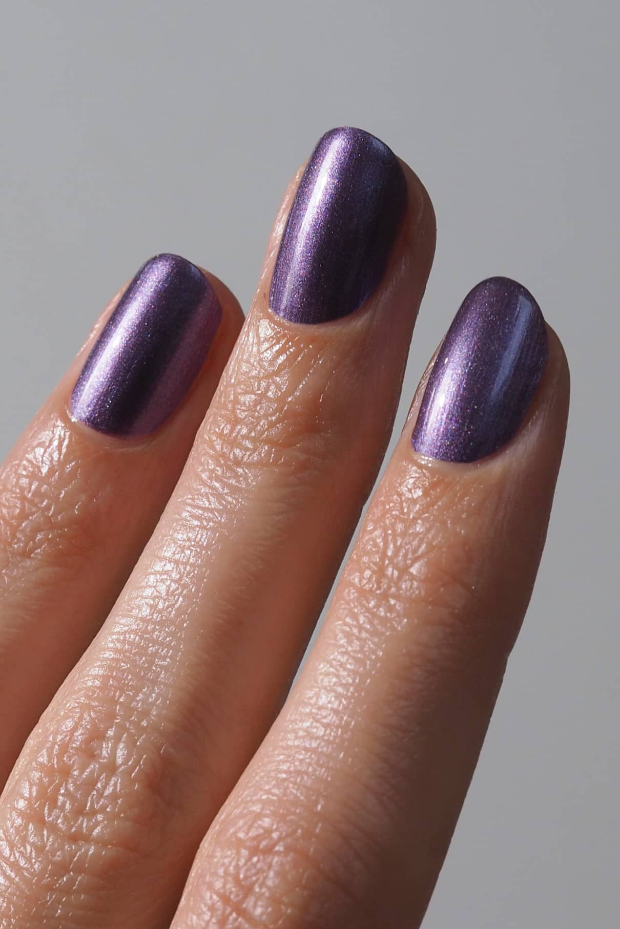 Nahaufnahme von drei Fingern mit kurzen, sauber manikürten Nägeln, die mit gitti no. 308, einem metallisch schimmernden violetten Nagellack, lackiert sind.