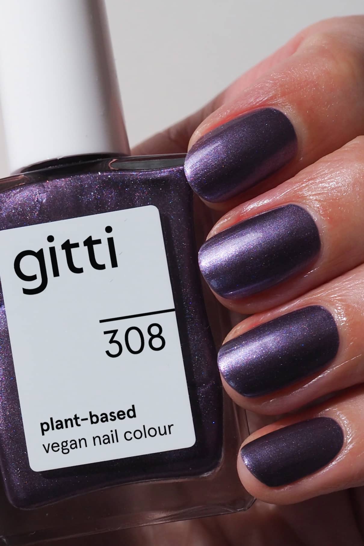 Eine Hand mit violettem Metallic-Schimmer-Nagellack in Violettton hält eine Flasche mit der Aufschrift gitti no. 308 pflanzliche vegane Nagelfarbe.