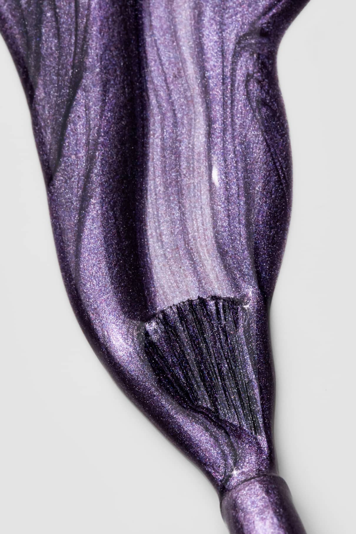 Nahaufnahme eines Pinsels, mit dem gitti no. 308, ein lilafarbener Metallic-Nagellack mit schimmerndem Finish, in einem sanften, geschwungenen Strich auf einer weißen Fläche.