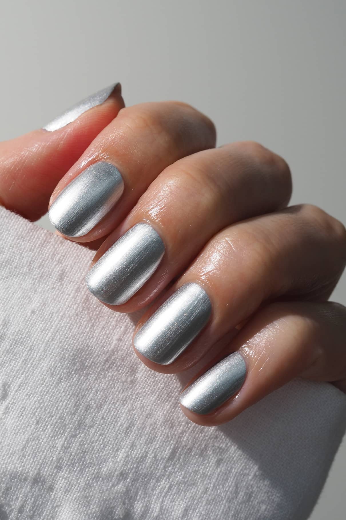 Eine Hand mit gepflegten Nägeln, lackiert in gitti no. 310, hält ein weißes Tuch und präsentiert einen faszinierenden Chrom-Effekt in metallischem Silber.