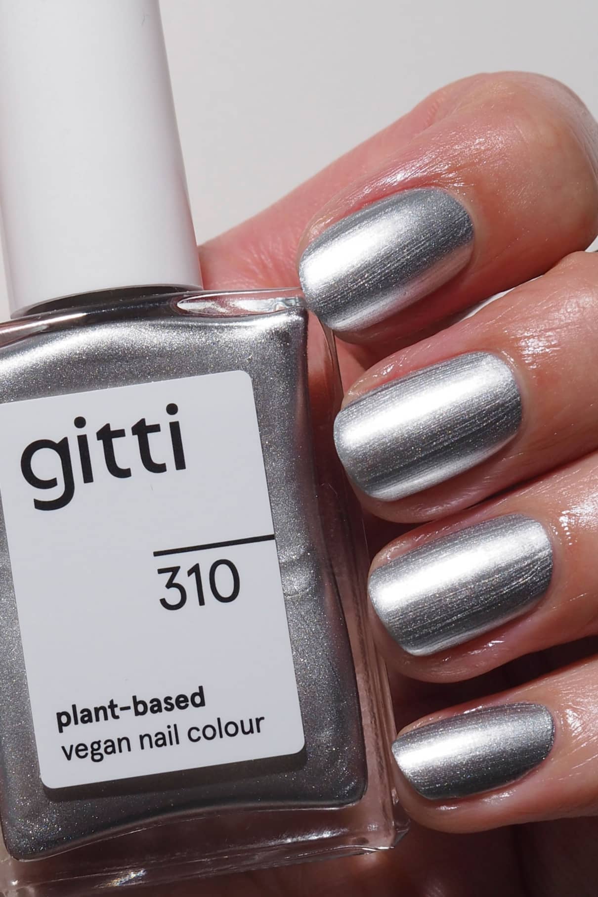 Eine Hand mit einer trendigen Maniküre mit Chromeffekt hält eine Flasche mit der Aufschrift gitti no. 310, eine pflanzliche, vegane Nagelfarbe mit silbernem Metallic-Finish.