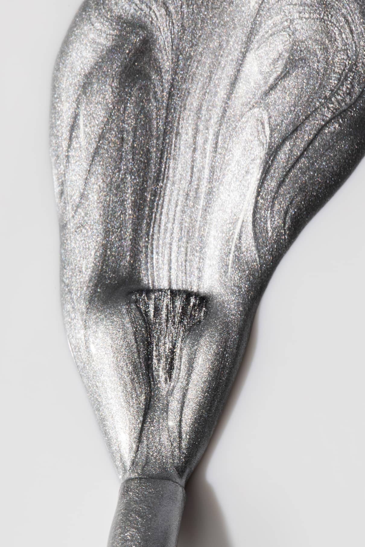 Eine Nahaufnahme von gitti no. 310 Silbermetallicfarbe mit Chrom-Effekt, dick aufgetragen und in strukturierten, wirbelnden Mustern auf weißem Untergrund verteilt.