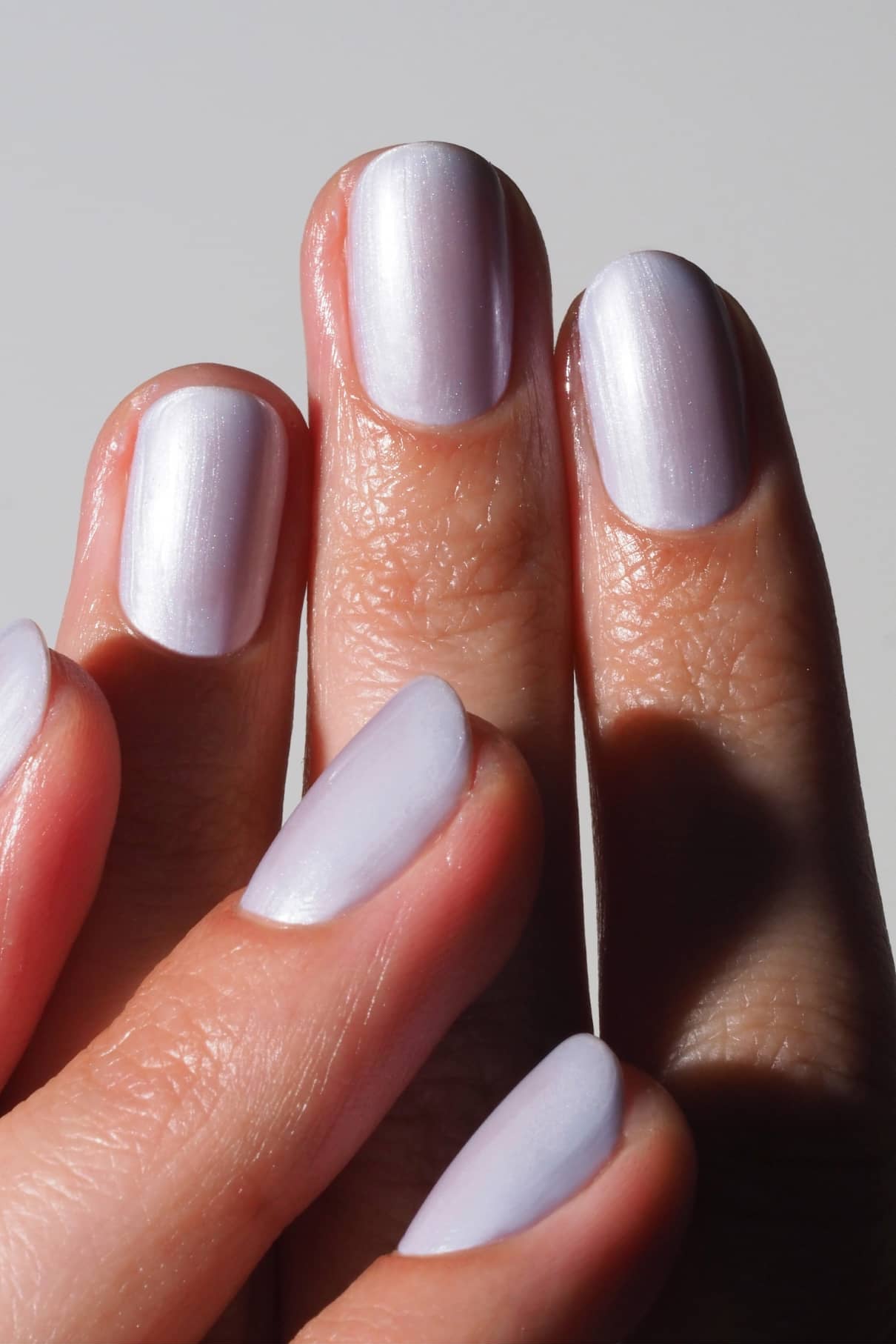 Nahaufnahme einer Hand mit sauber manikürten Nägeln, lackiert mit gitti no. 311, einem schimmernden lilafarbenen Lack mit Metallic-Finish, vor einem schlichten Hintergrund.
