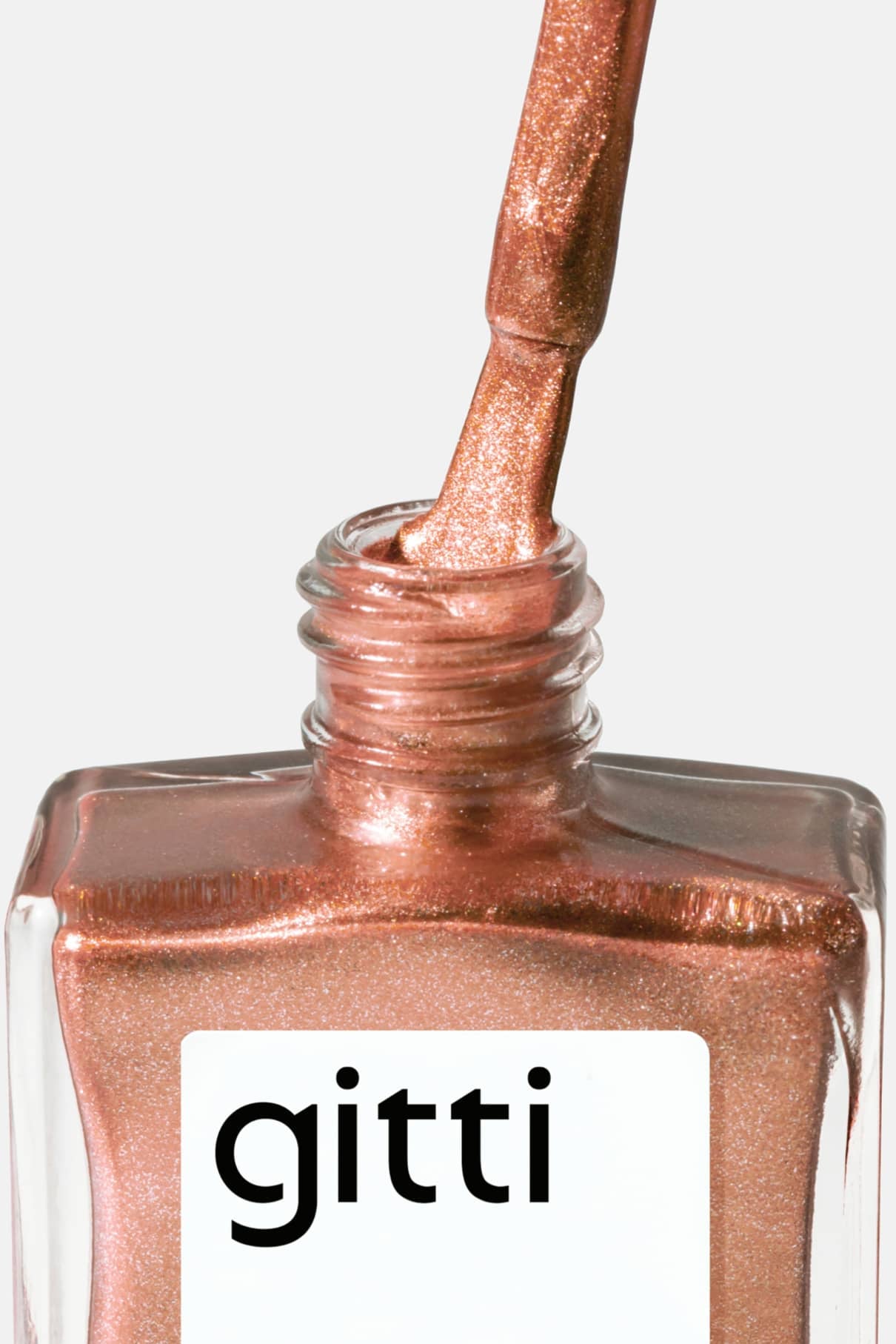 Ein Pinsel, getaucht in gitti no. 312 metallic apricot-roségoldfarbener Nagellack schwebt über einer offenen quadratischen Glasflasche mit der Aufschrift gitti.