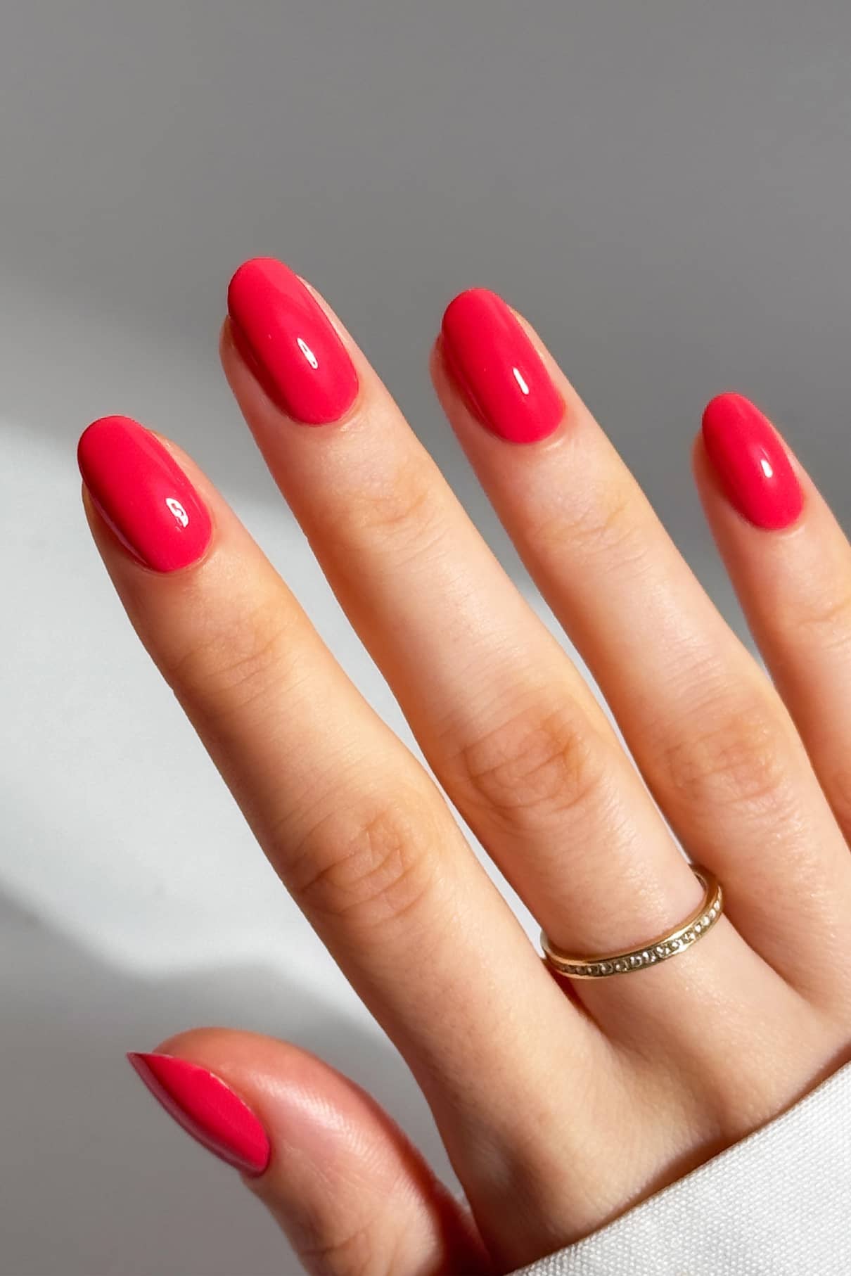 Eine Hand mit sauber manikürten Nägeln, lackiert in gitti no. 038, die einen dünnen Goldring am Ringfinger trägt, strahlt Wärme und Tiefe vor einem schlichten Hintergrund aus.