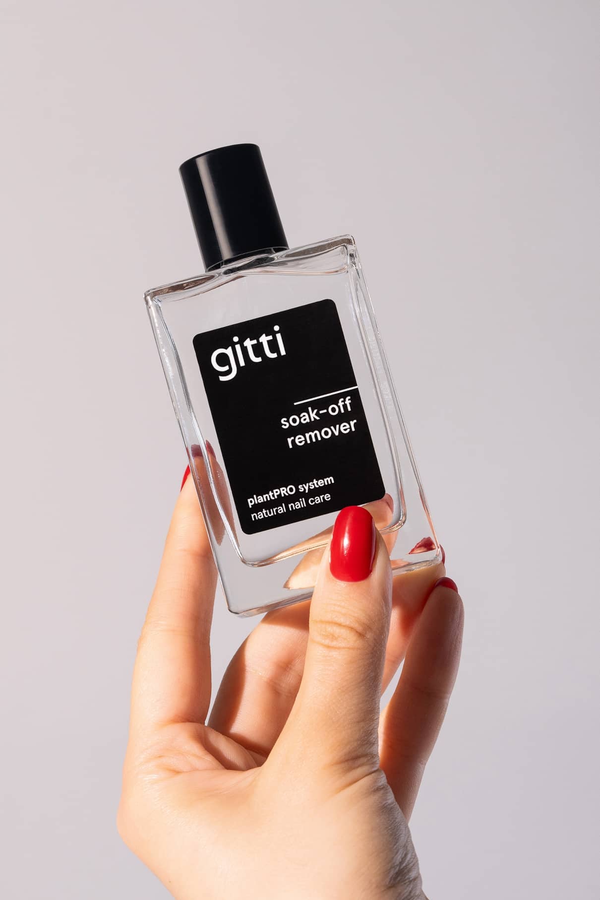 Eine Hand mit rot lackierten Nägeln hält eine durchsichtige rechteckige Flasche mit der Aufschrift plantPRO Refill Set natural nail care vor einem schlichten hellen Hintergrund.