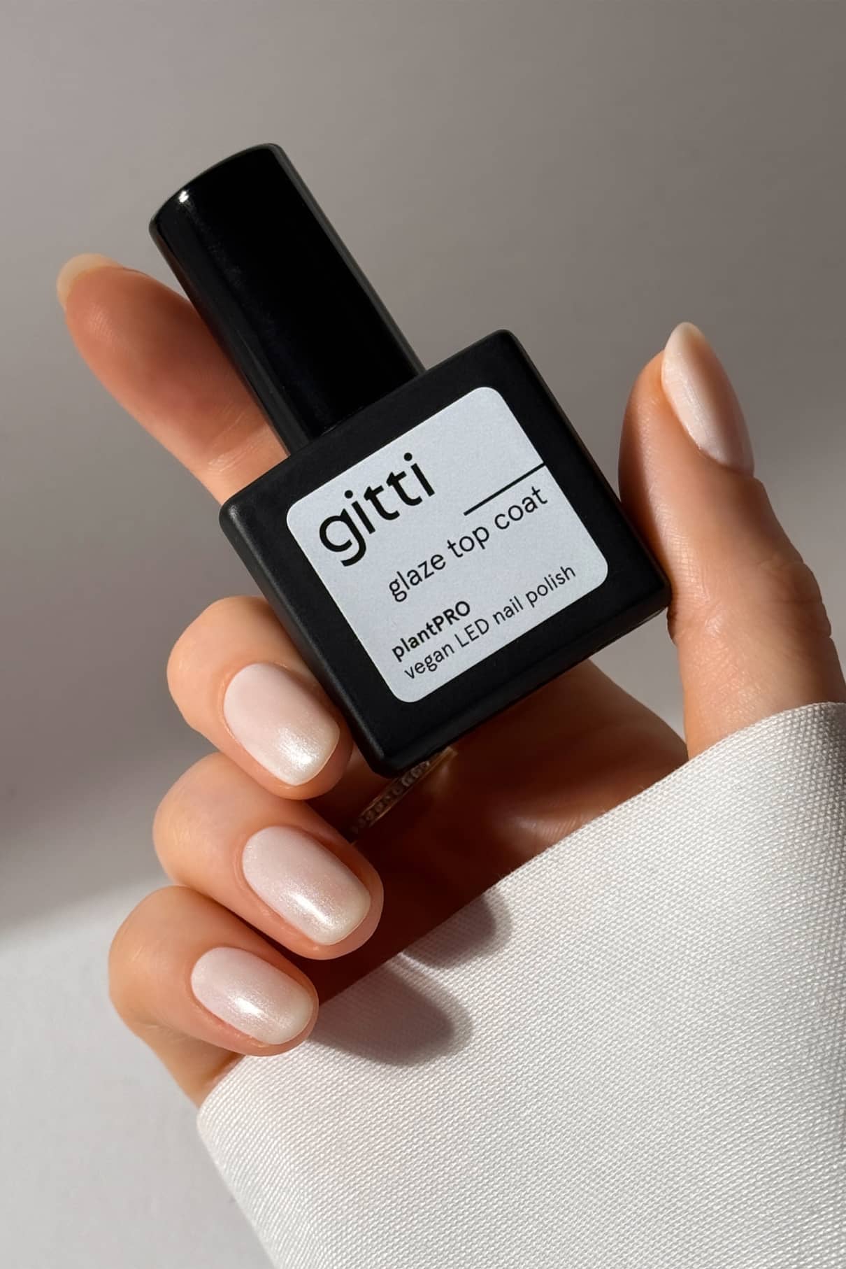 Eine Hand mit sauber manikürten, blassrosa Nägeln hält eine Flasche plantPRO Refill Set vor einem neutralen Hintergrund, perfekt, um Ihren Look nach dem Auftragen des Base Coat zu vollenden.