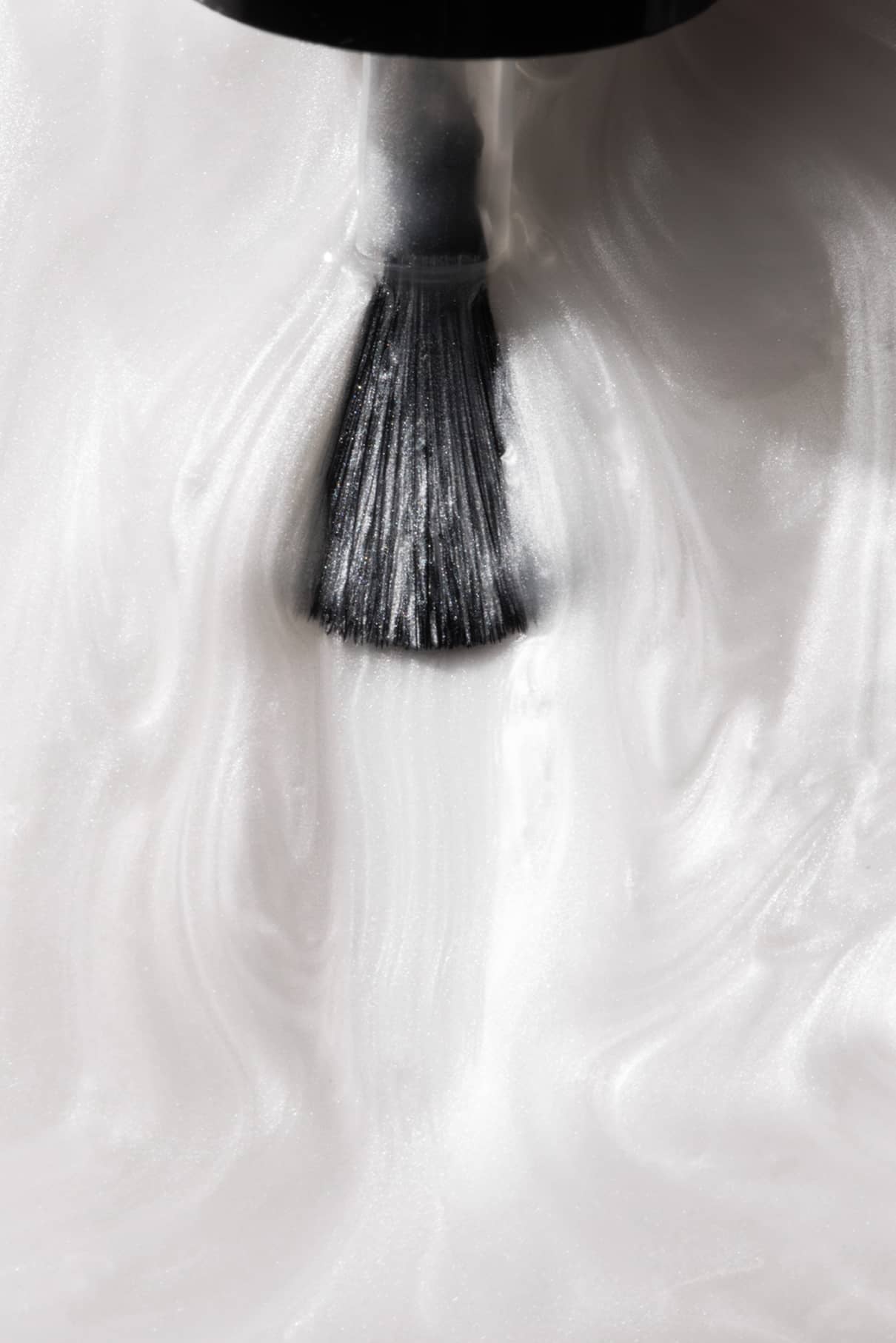 Eine Nahaufnahme eines schwarzen Nagellackpinsels, der den weißen plantPRO Glaze Top Coat in wirbelnden Mustern für Gel-Nägel und ein schimmerndes Finish verteilt.