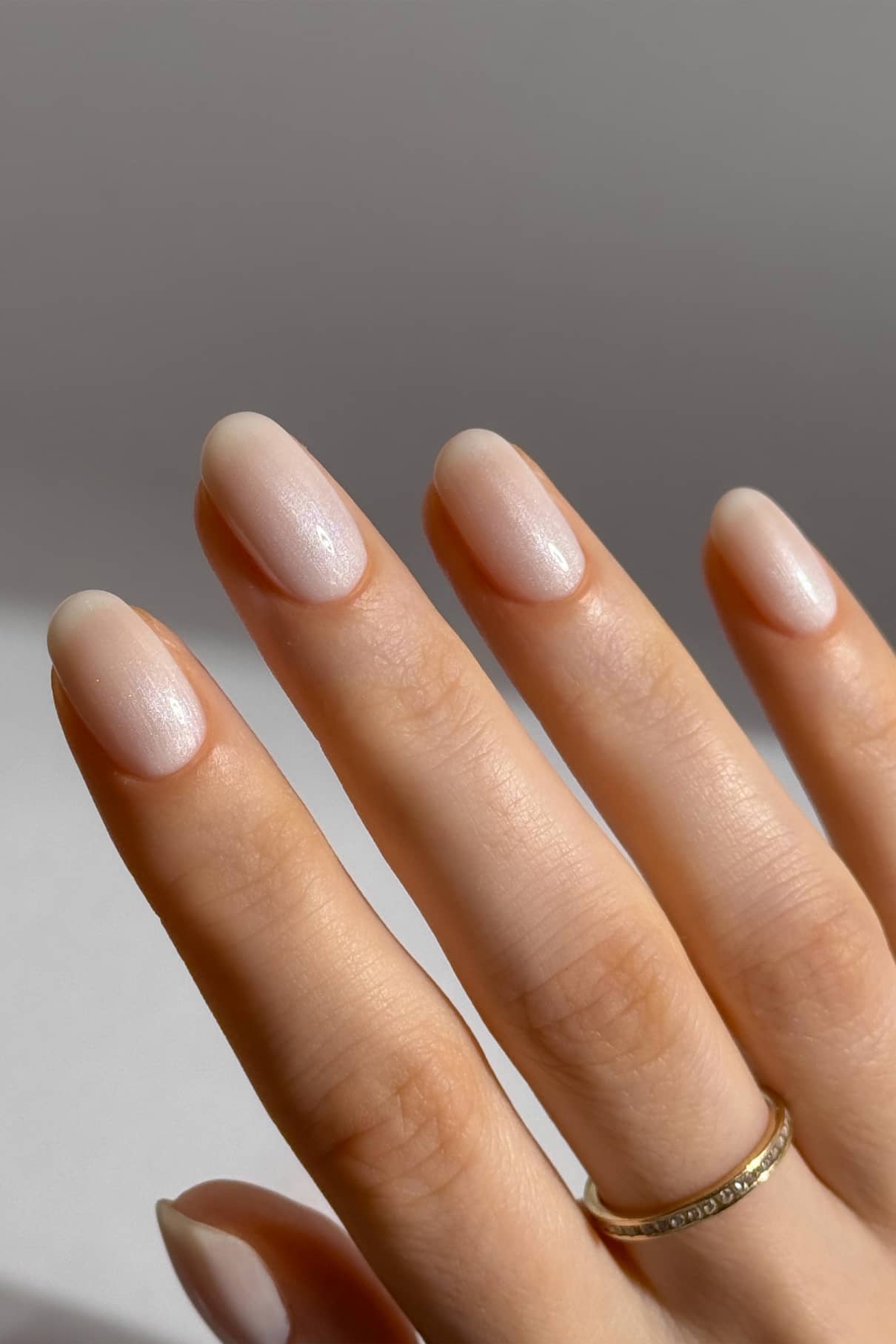 Eine Hand mit kurzen, ovalen Nägeln, die in hellem Rosa lackiert und mit plantPRO Glaze Top Coat für einen schimmernden Effekt veredelt wurden. Ein schlichter Goldring ziert den Ringfinger und sorgt für einen Gel-Nagel-Look.
