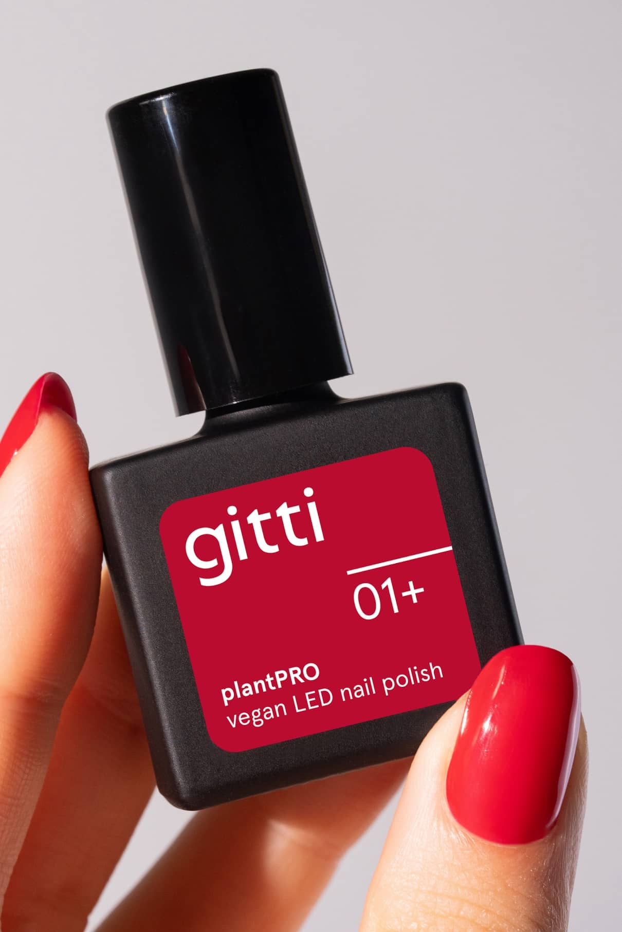 Eine Hand mit rot lackierten Nägeln hält eine Flasche von gitti no. 01+, die das intensive Rot des veganen LED-Nagellacks zur Schau stellt.