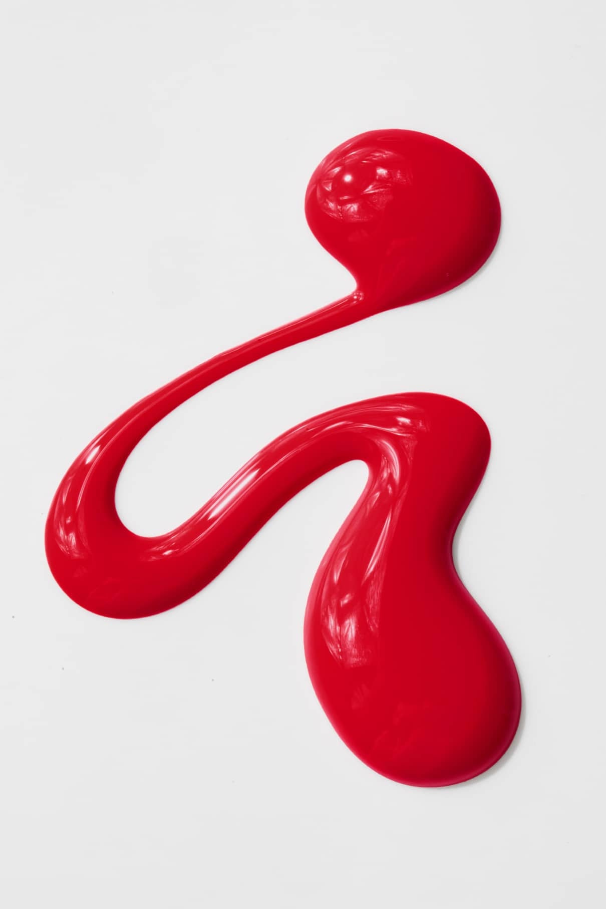 Ein Wirbel aus glänzender gitti no. 01+ roter Flüssigfarbe auf weißem Hintergrund schafft eine abstrakte Form mit sanften Kurven und einer einzelnen Schleife.