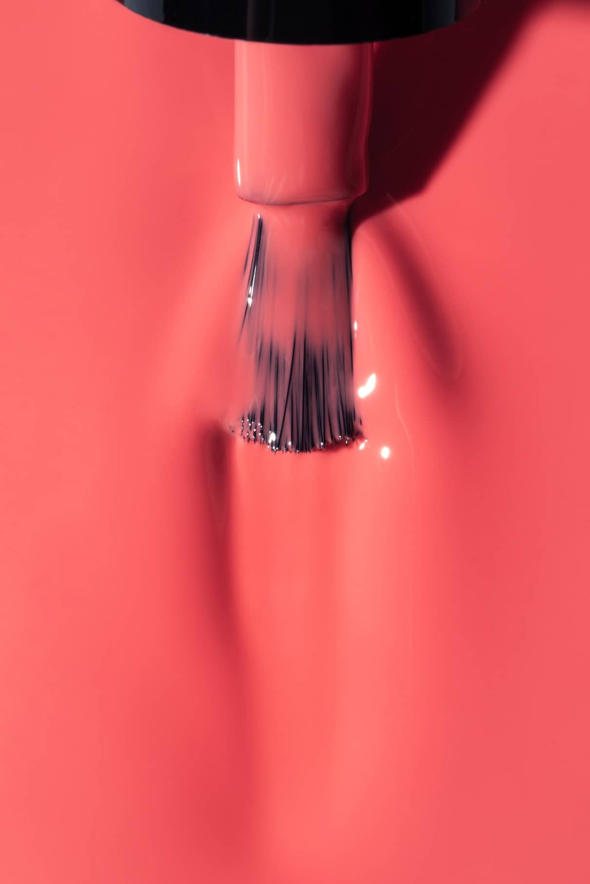 Eine Nahaufnahme eines Nagellackpinsels, der gitti no. 02+, ein leuchtendes Korallrosa mit einem wärmeren Unterton, auf eine Fläche auf.