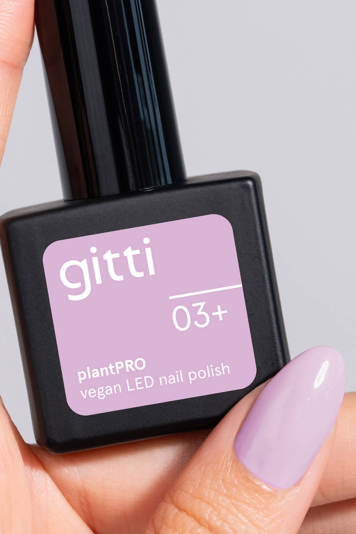 Eine Hand mit hellviolett lackierten Nägeln in romantischem Lavendel hält eine Flasche gitti no. 03+ pflanzlichen, veganen LED-Nagellack, perfekt für alle mit wärmeren Untertönen.